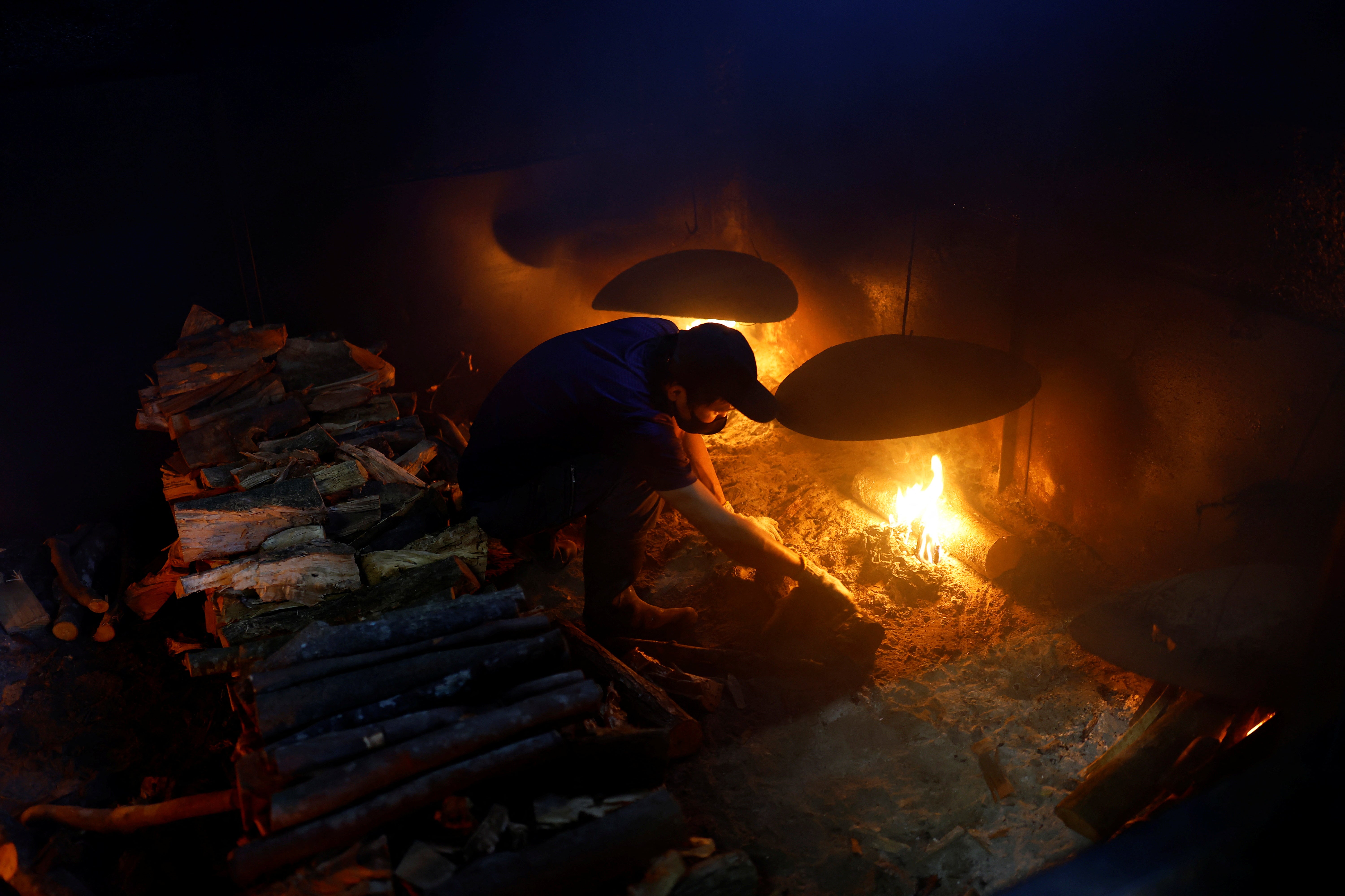 A worker uses firewood in a furnace to smoke the boiled fillets in the factory