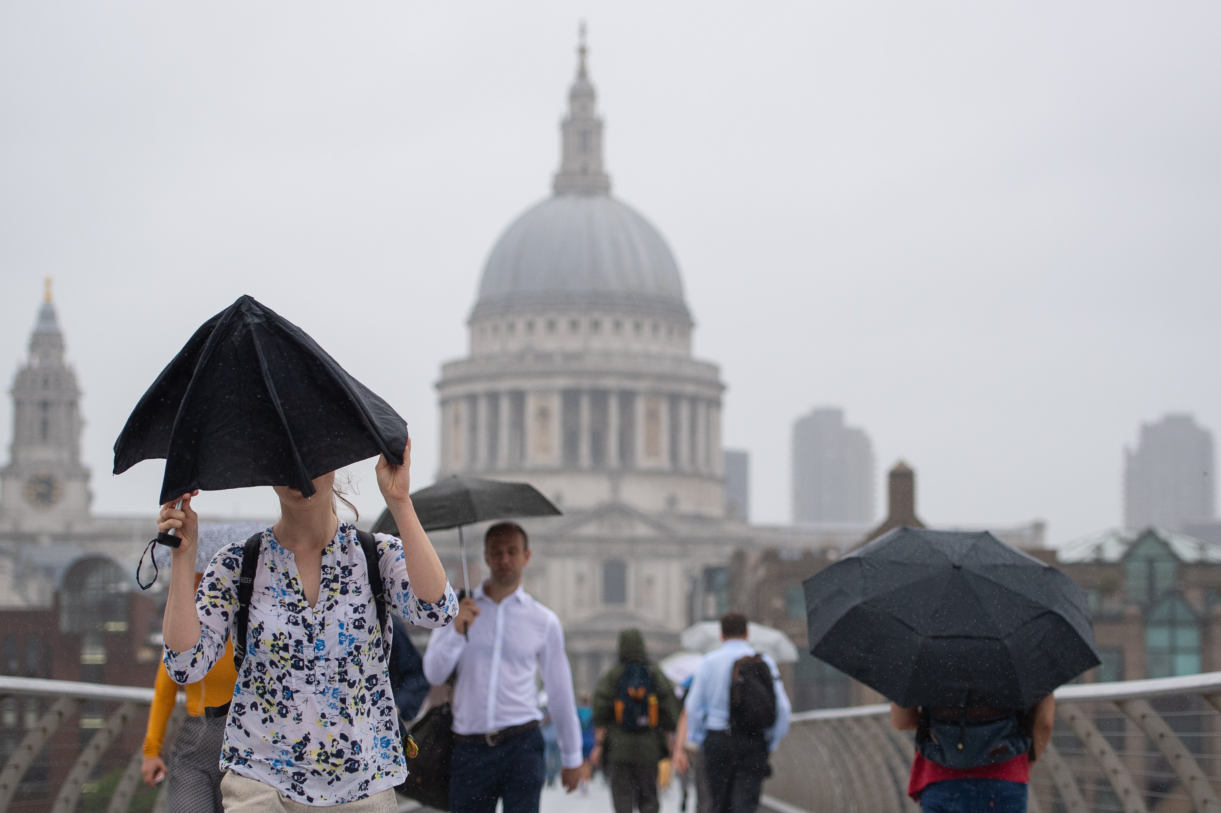 Pedestrians shelter under umbrellas as they cross the Millennium Bridge (Dominic Lipinski/PA)