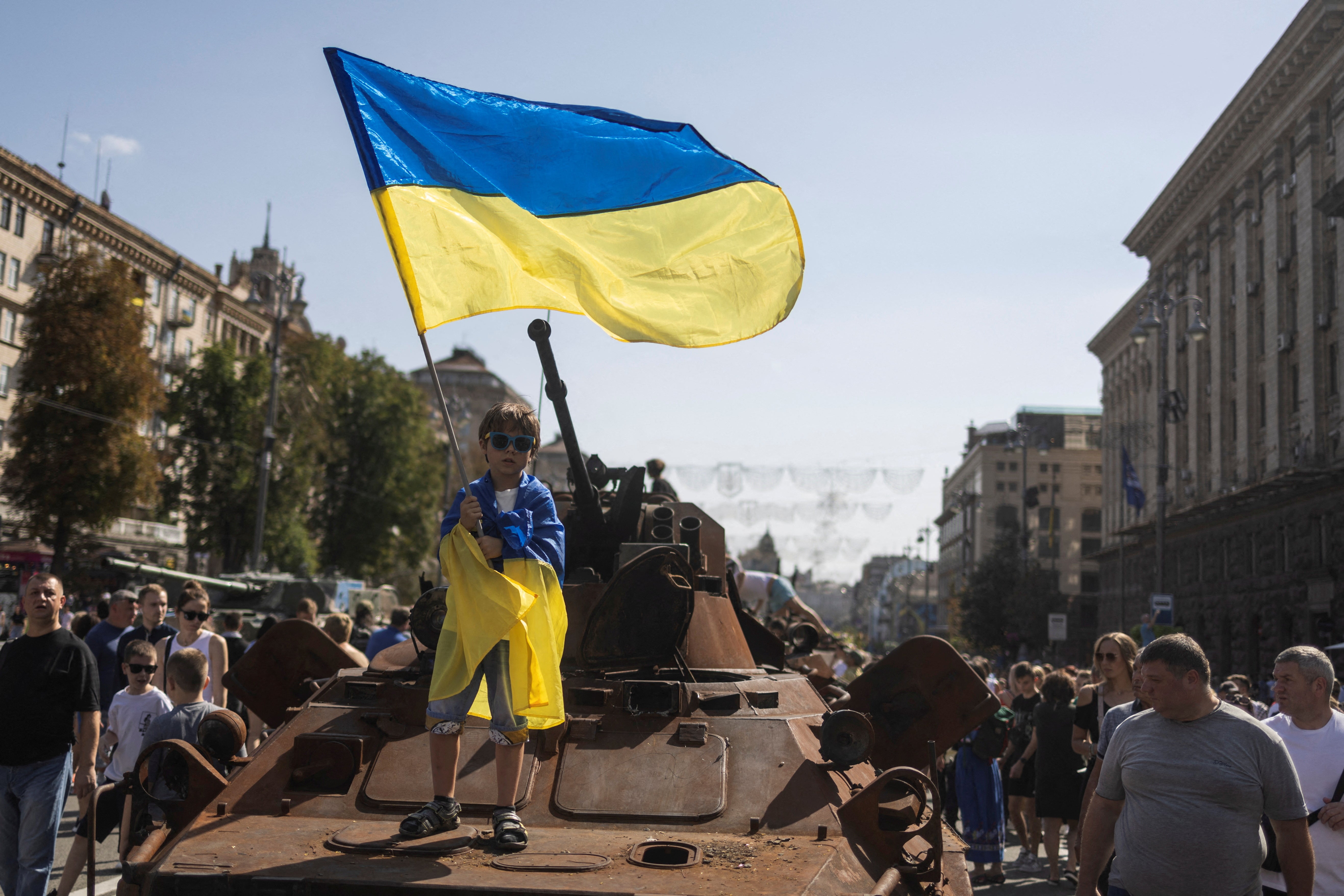 A boy waves a national flag atop an armoured van at an exhibition of destroyed Russian military vehicles