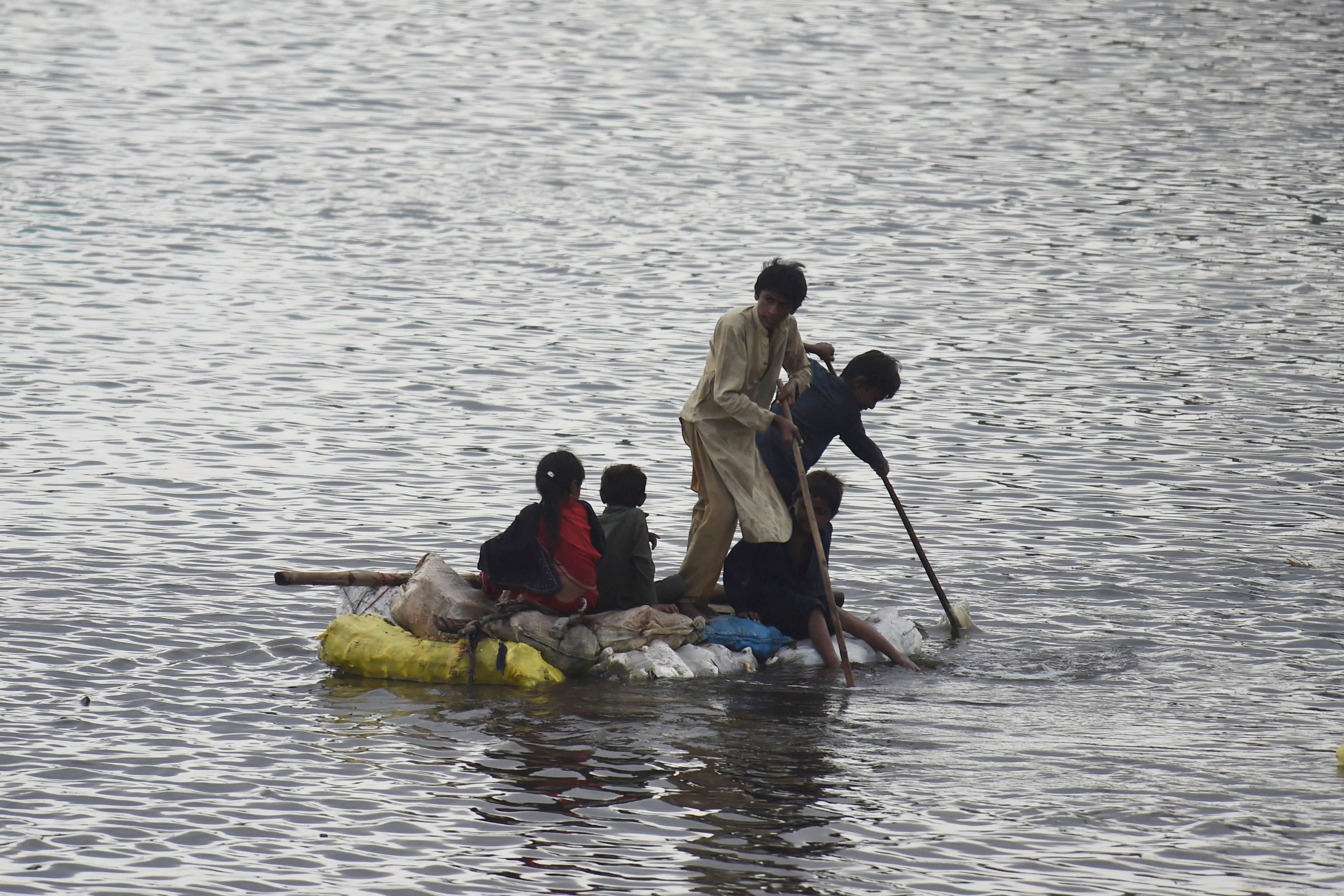 Children use a raft to make their way in a flooded area after heavy monsoon rains on the outskirts of Sukkur, Sindh province, on August 27, 2022