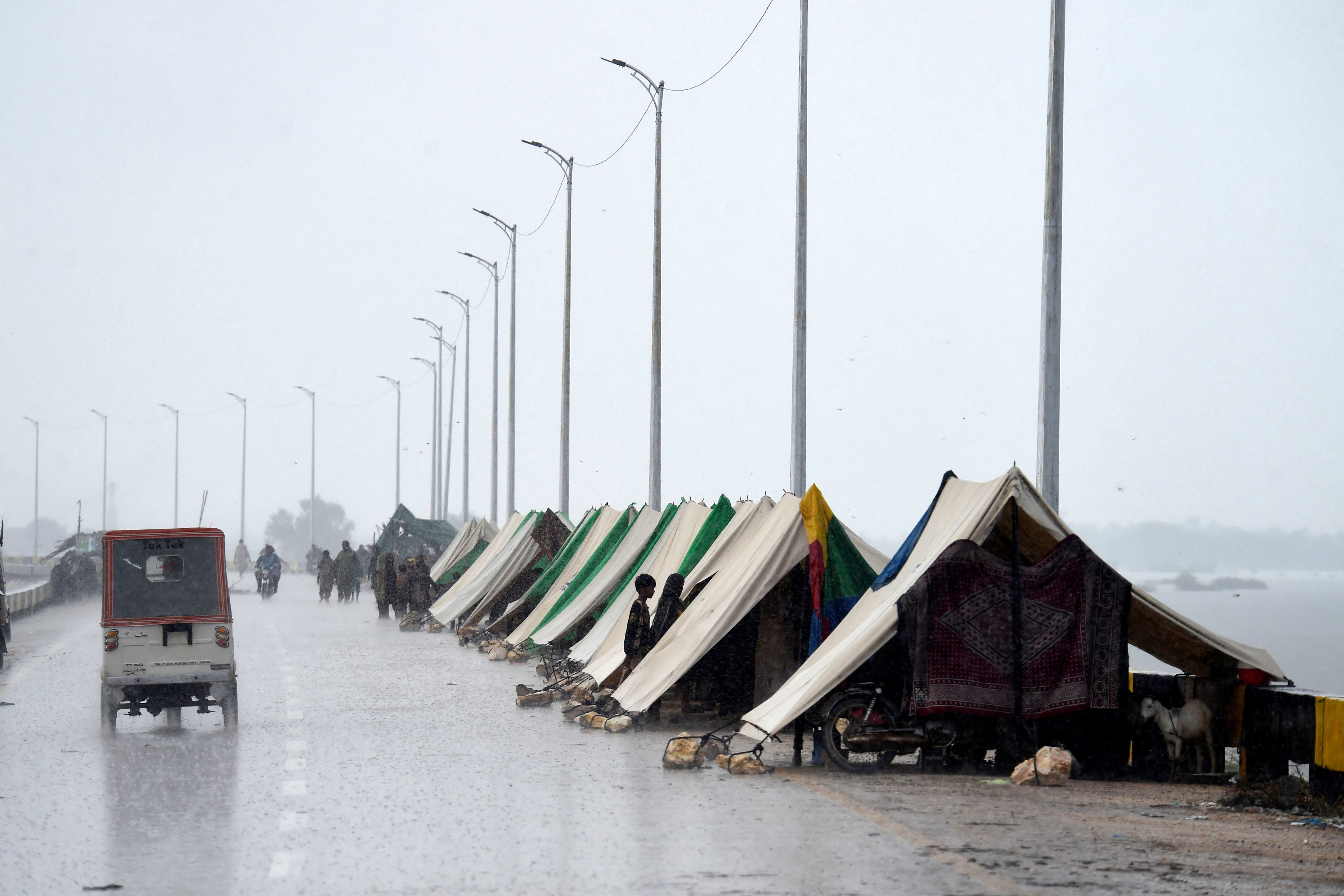 An auto-rickshaw drives past temporary tents of people who fled their flood-hit homes set along a road in Sukkur, Sindh province, on 27 August, 2022