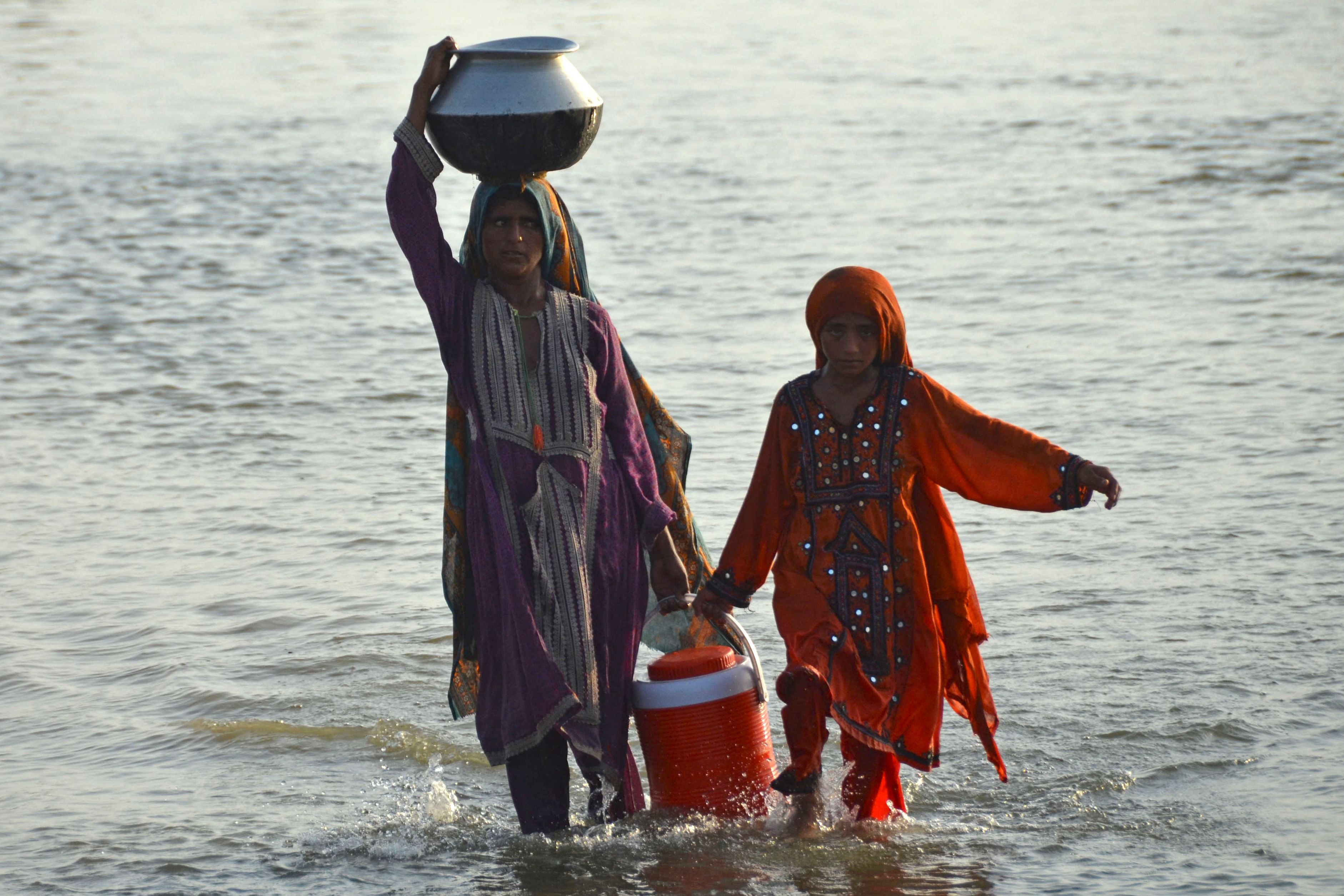 Flood-affected women carry drinking water in containers after fleeing from their homes following heavy monsoon rains in the Sohbatpur area in Jafarabad district of Balochistan province