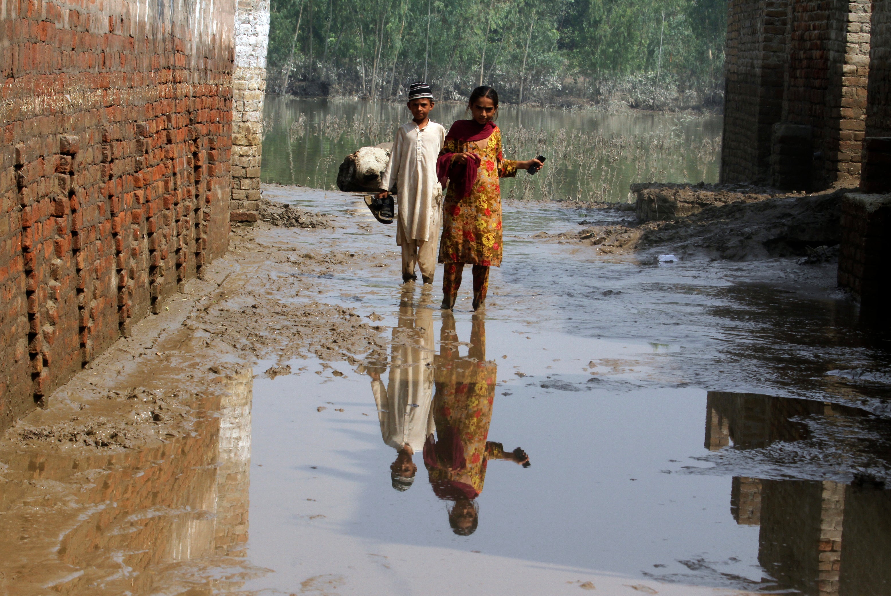 A boy and girl wade through mud near their flood-hit home in Charsadda, Pakistan (Mohammad Sajjad/AP)