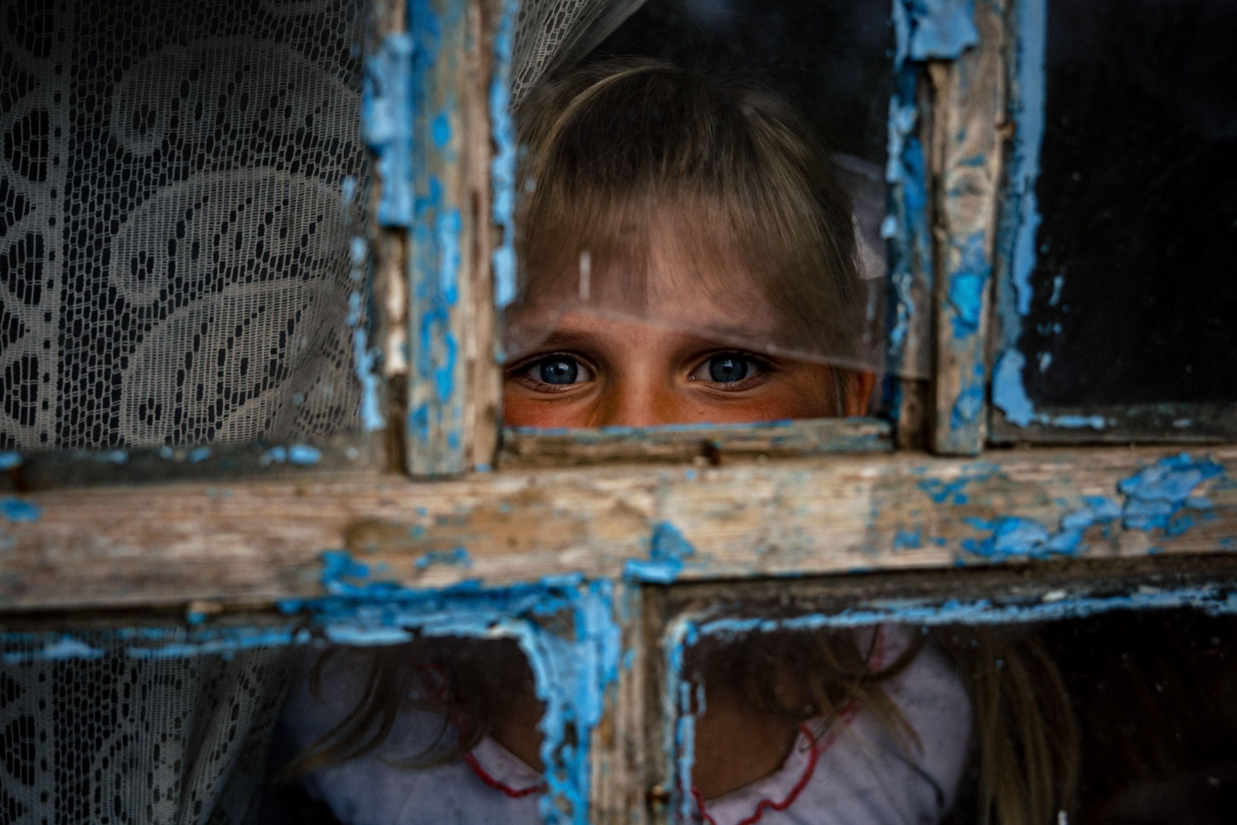 A nine-year-old girl looks through a shrapnel-broken window at her home in Pokrovske, Ukraine, near the front line