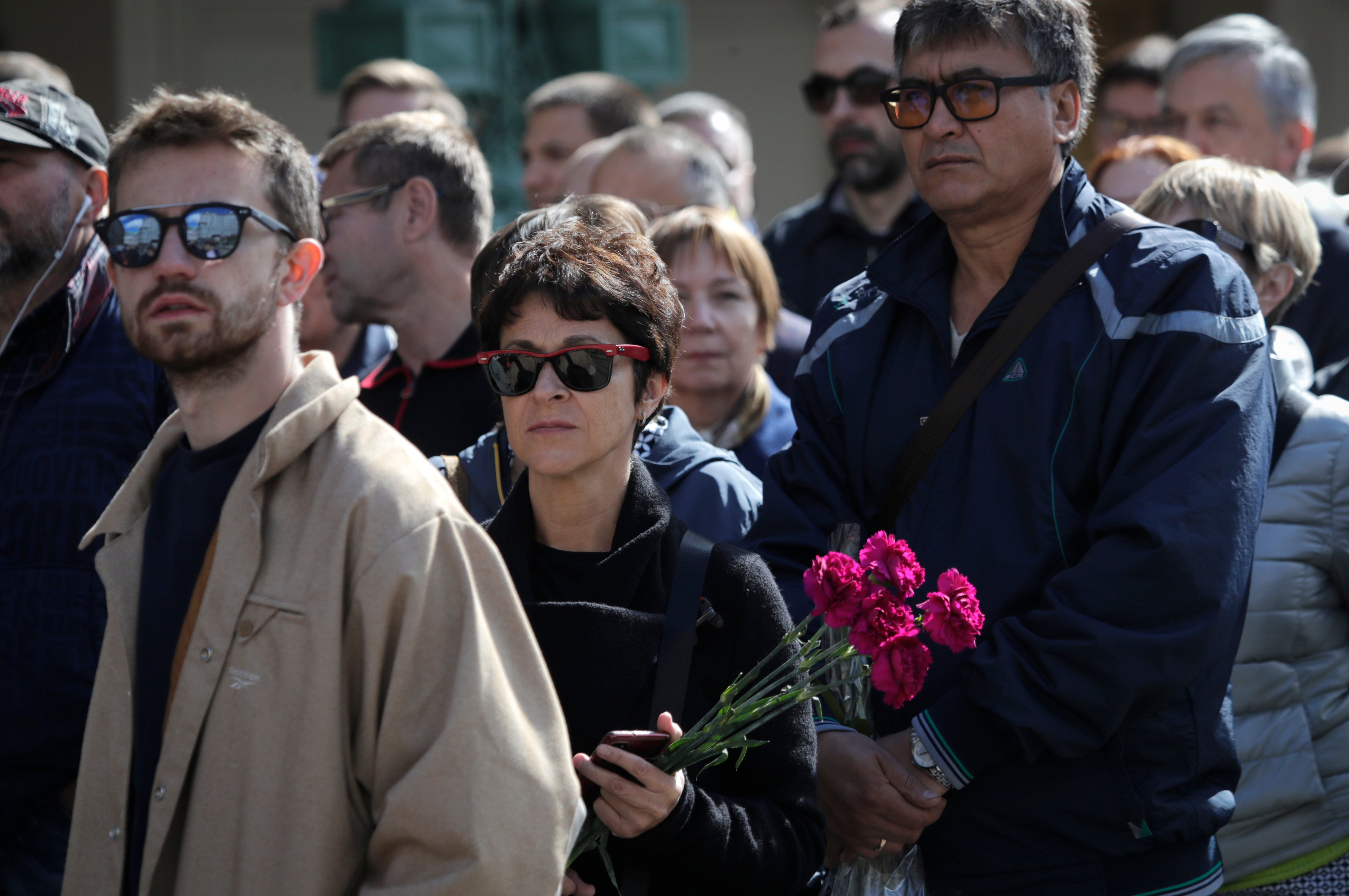 A woman holding flowers looks on as she lines up to say goodbye