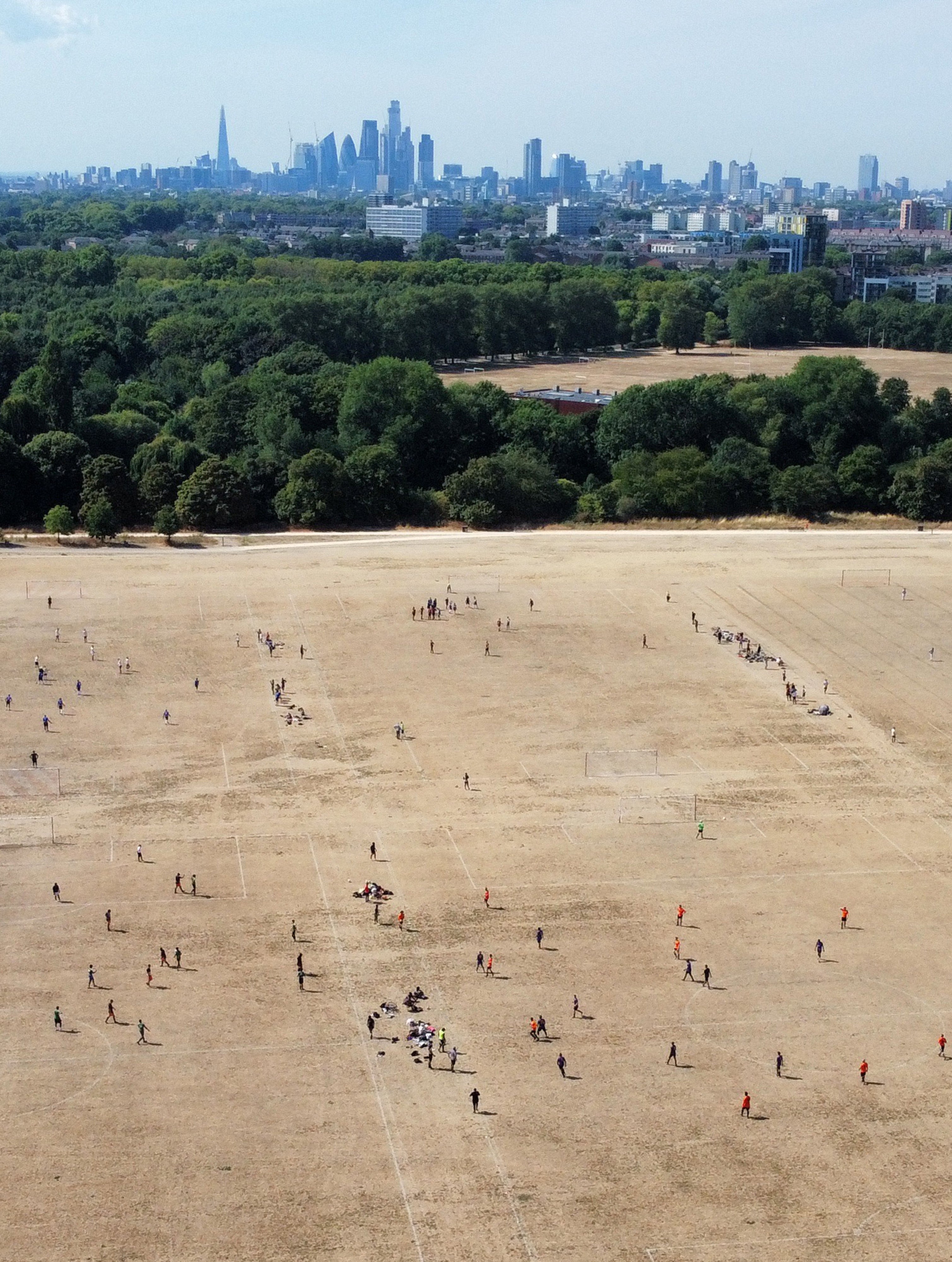 People play Sunday league amateur football matches on parched grass pitches during a heatwave, with the central London skyline seen behind, at Hackney Marshes, in London, Britain, August 14, 2022