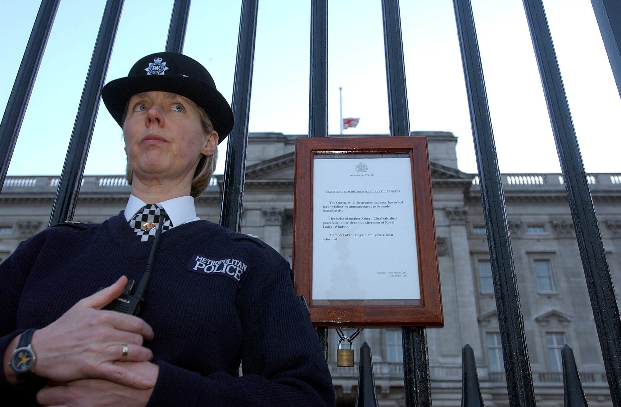 A police officer stands next to the announcement of the death of the Queen Mother as the Union flag flies at half mast over Buckingham Palace (Kirsty Wigglesworth/PA)