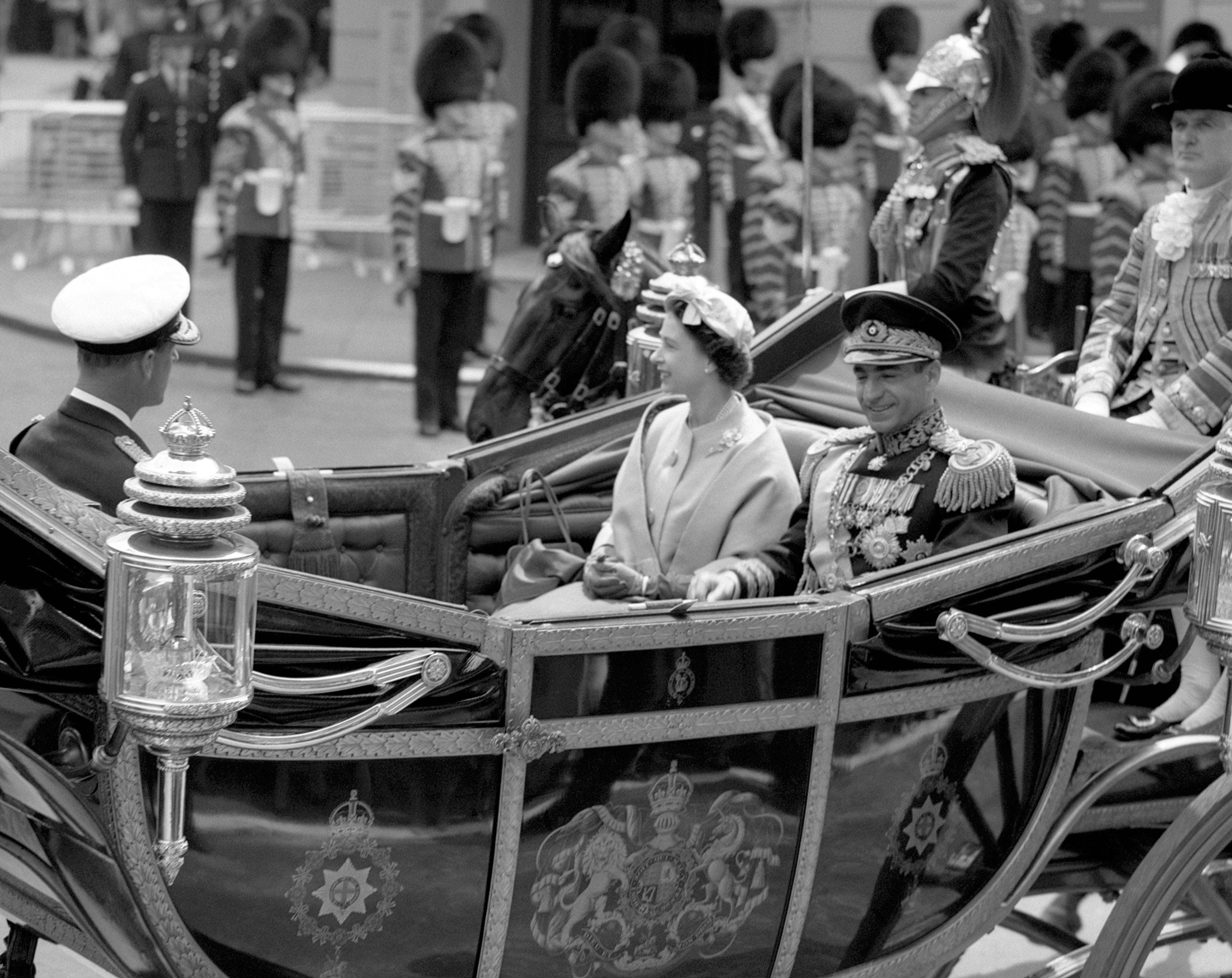 The Shah of Iran sits with Queen Elizabeth II in an open carriage as they drive with the Duke of Edinburgh to Buckingham Palace from Victoria Station