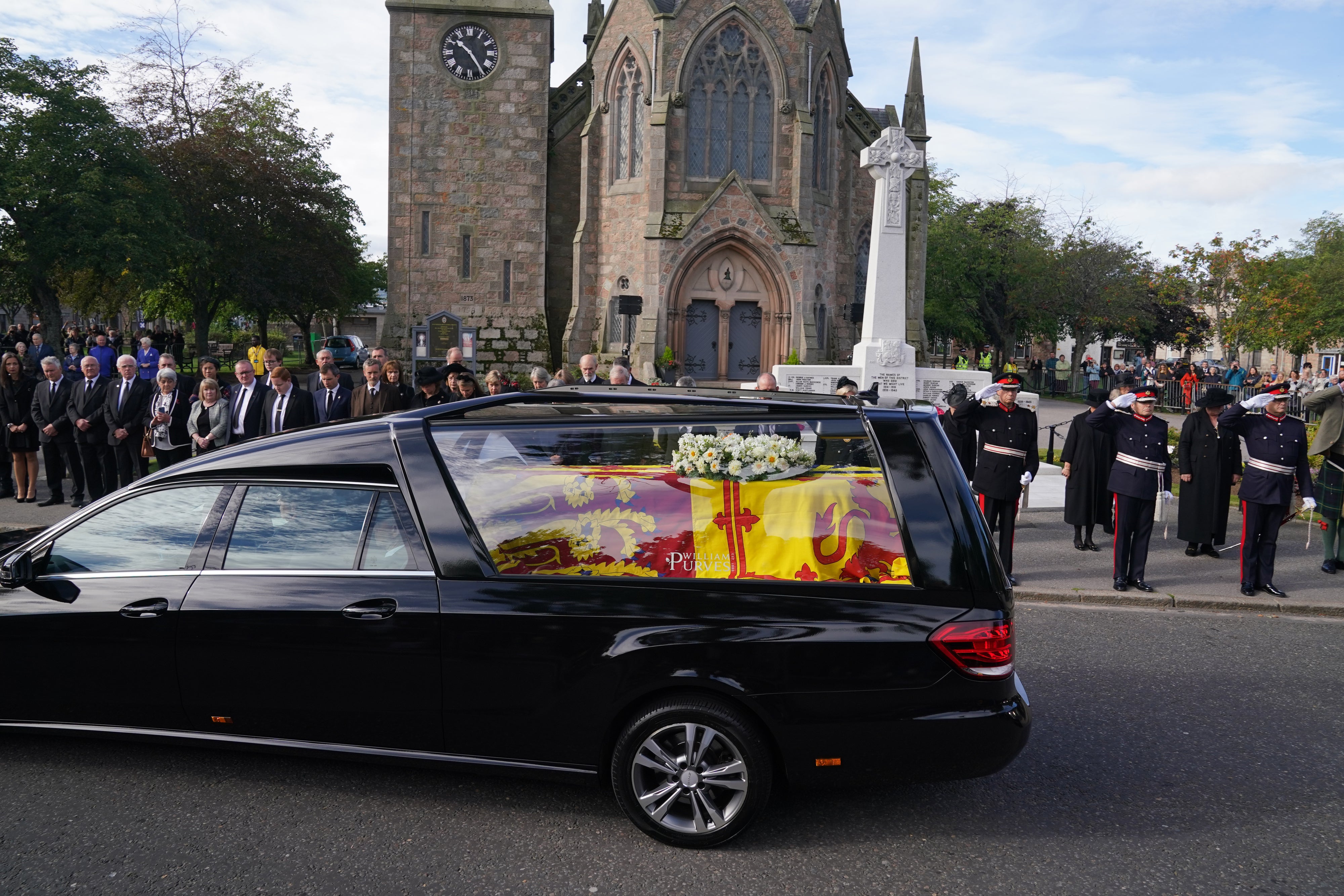 Members of the military salute the hearse carrying the coffin of Queen Elizabeth II, draped with the Royal Standard of Scotland, passing through Ballater as it continues its journey to Edinburgh from Balmoral (Andrew Milligan/PA)