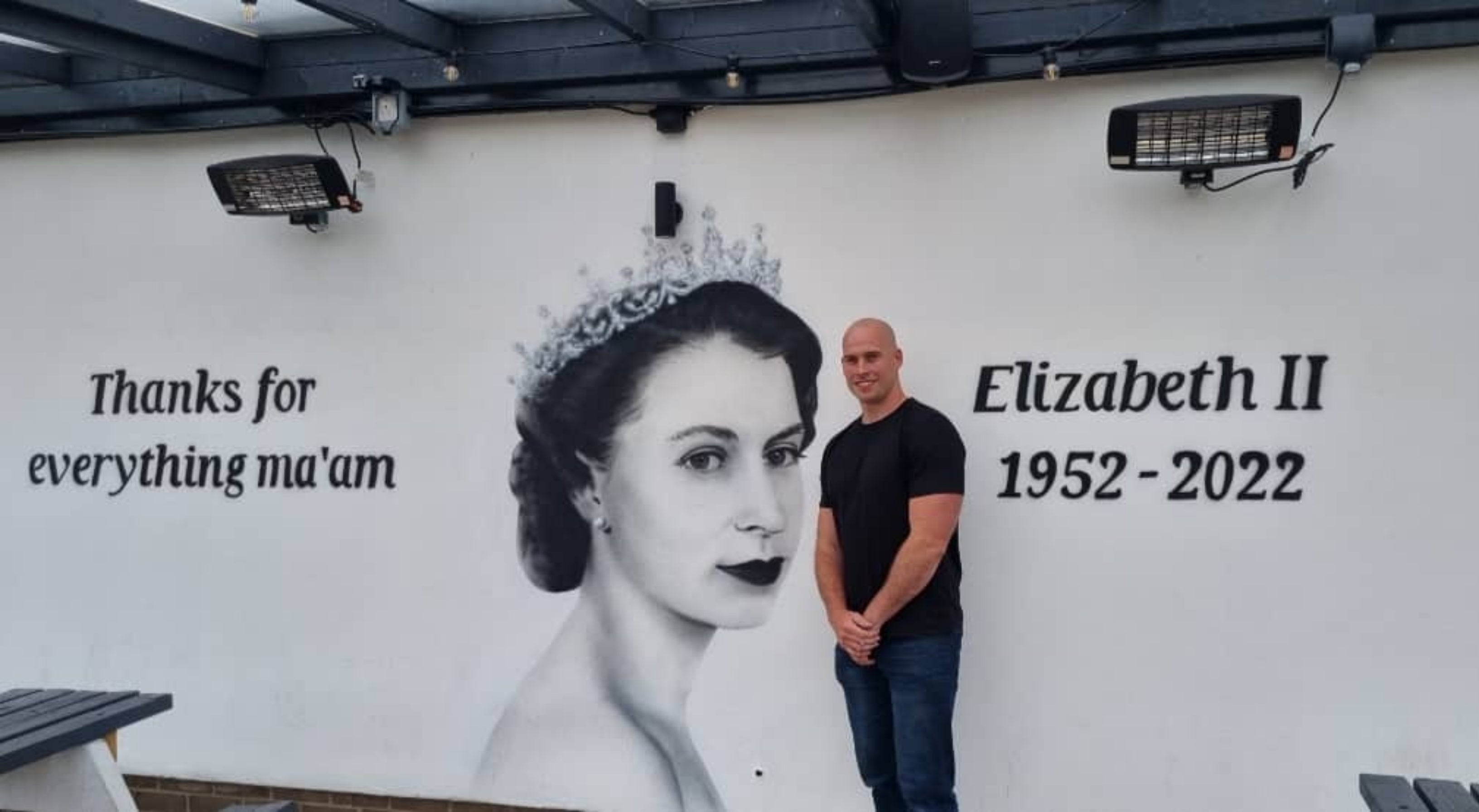 Scott Wilcock stood next to his mural to the Queen at the Queens Arms pub in Manchester (Scott Wilcock/PA)