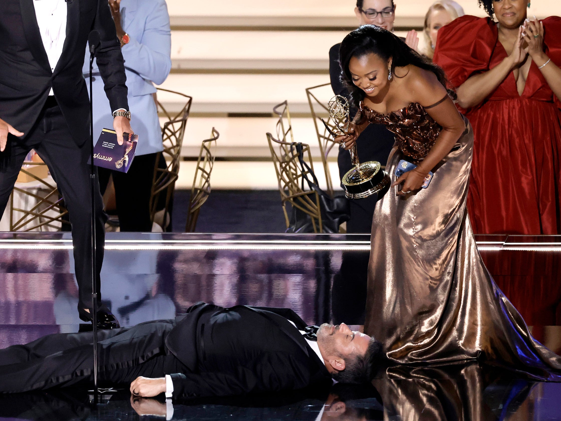 Quinta Brunson (R) accepts Outstanding Writing for a Comedy Series for "Abbott Elementary" from Will Arnett (L) while Jimmy Kimmel lies onstage during the 74th Primetime Emmys at Microsoft Theater on September 12, 2022 in Los Angeles, California. (Photo by Kevin Winter/Getty Images)