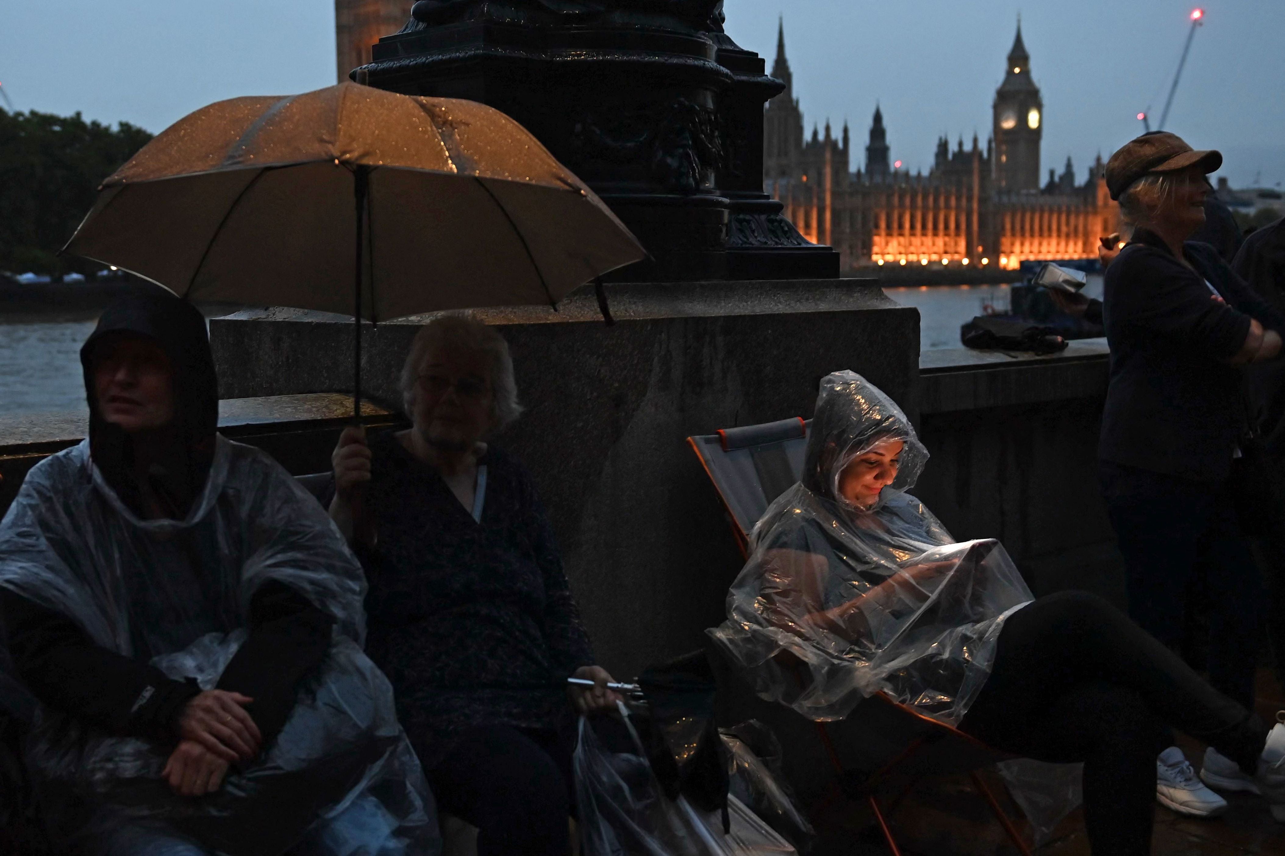 Members of the public queue in the rain along the south bank of the River Thames