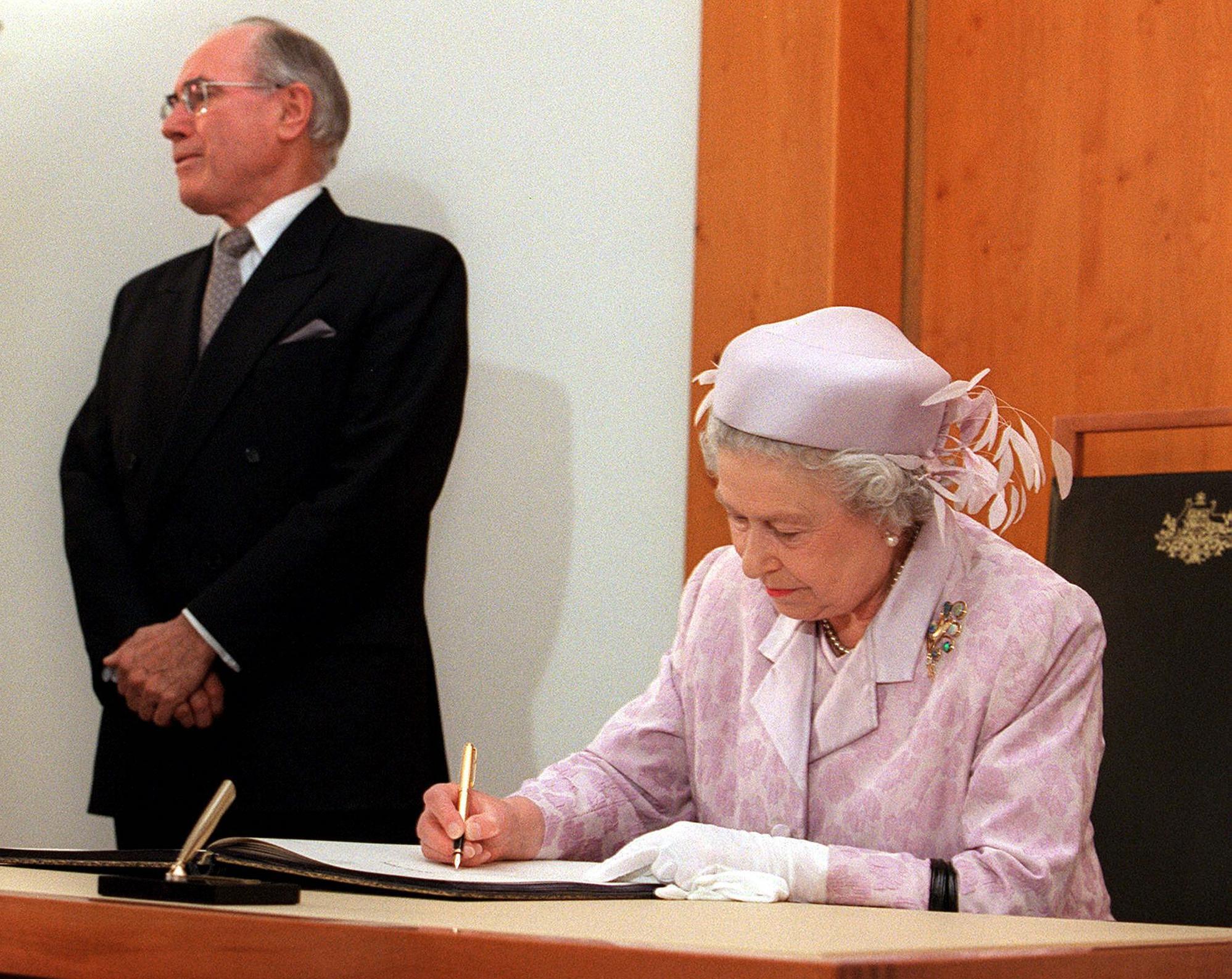 Queen Elizabeth II signs the visitor's book at Parliament House in Canberra 27 March 2000 as Australian Prime Minister John Howard stands in the background