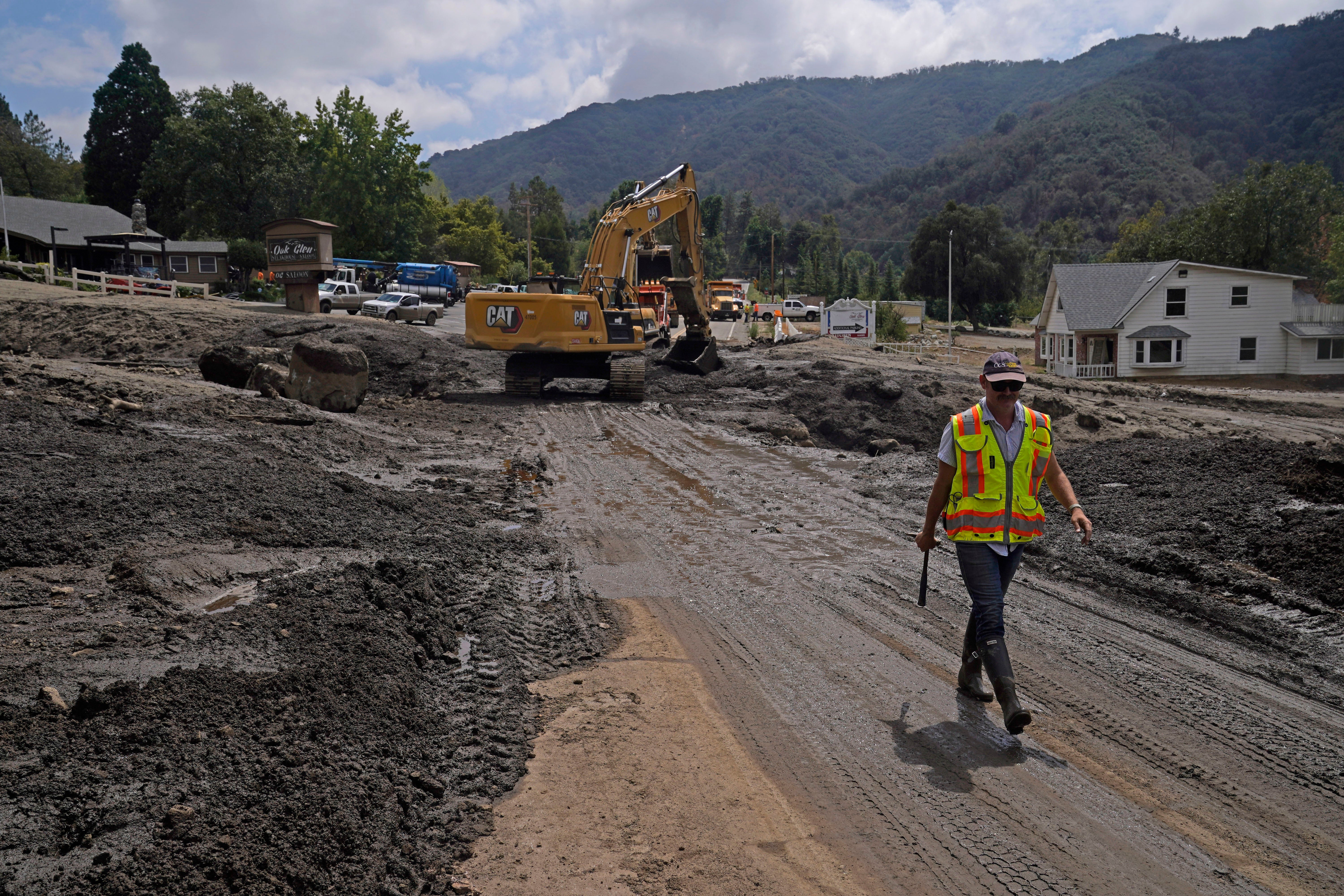 Workers clear mud from a road on Tuesday after mudslides poured down into southern California communities this week