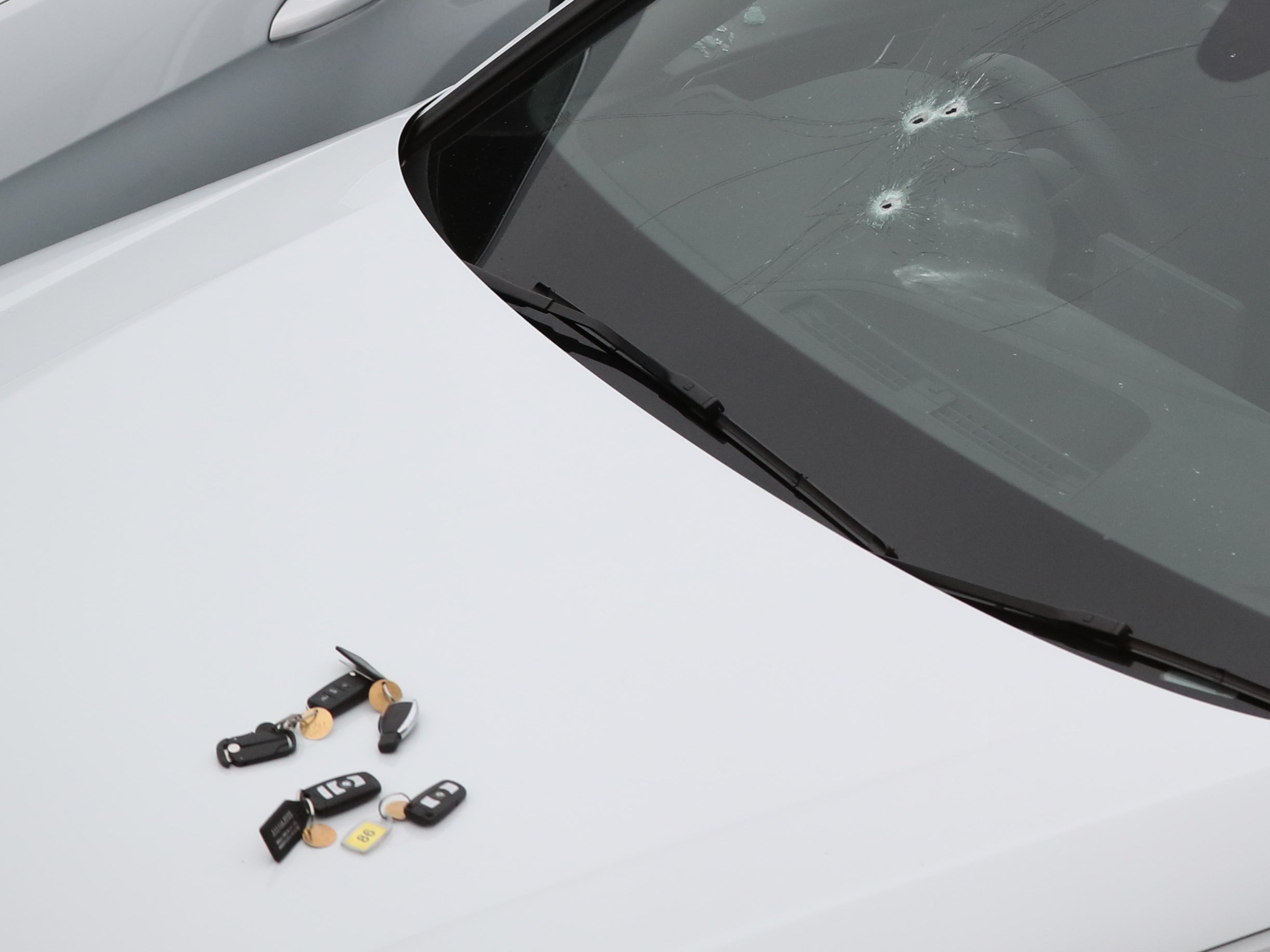 A silver Audi with bullet holes in its windscreen and several sets of keys on its bonnet at the scene