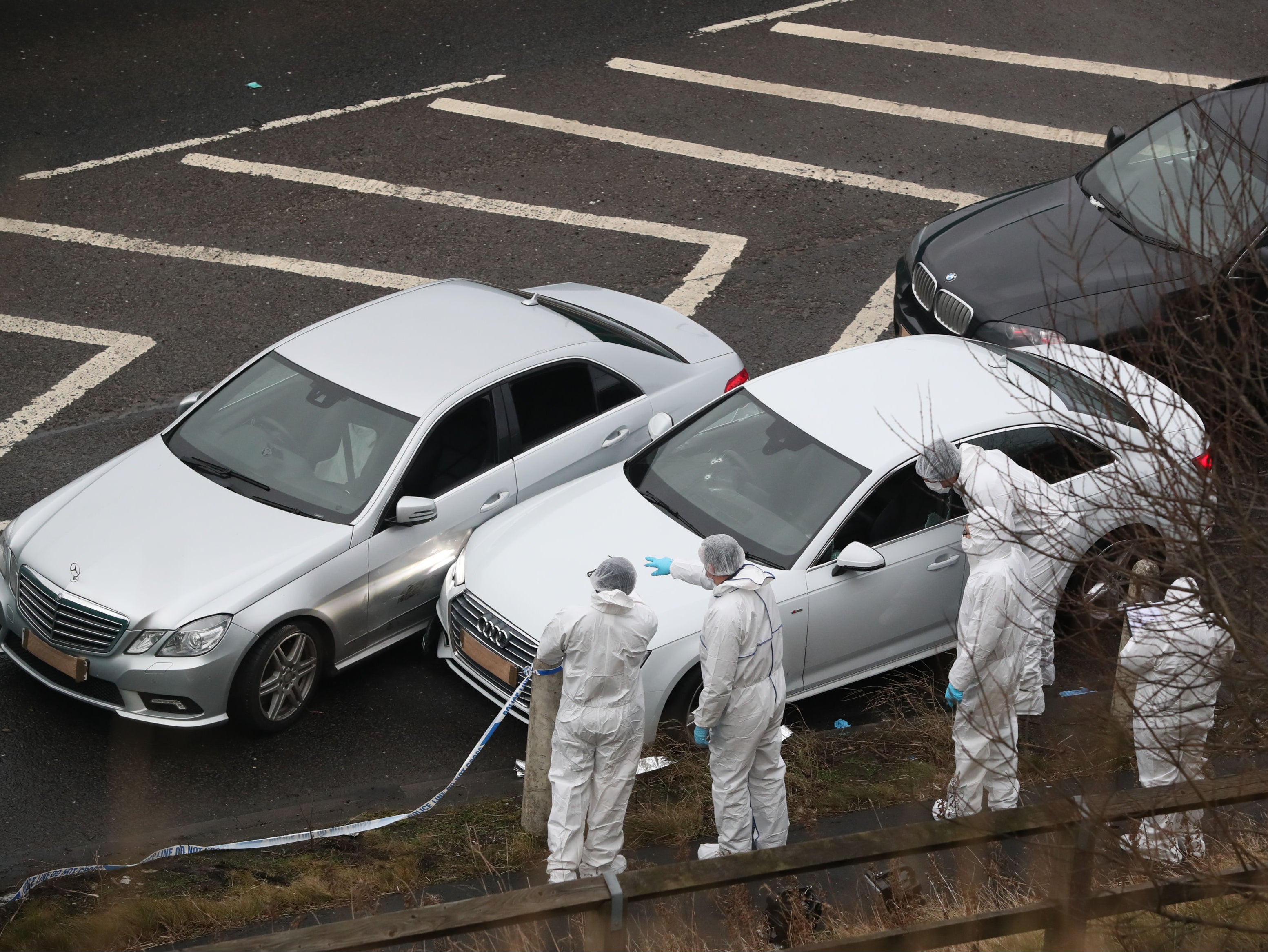 Police forensics officers examine a silver Audi with bullet holes in its windscreen at the scene near junction J24 of the M62 in Huddersfield
