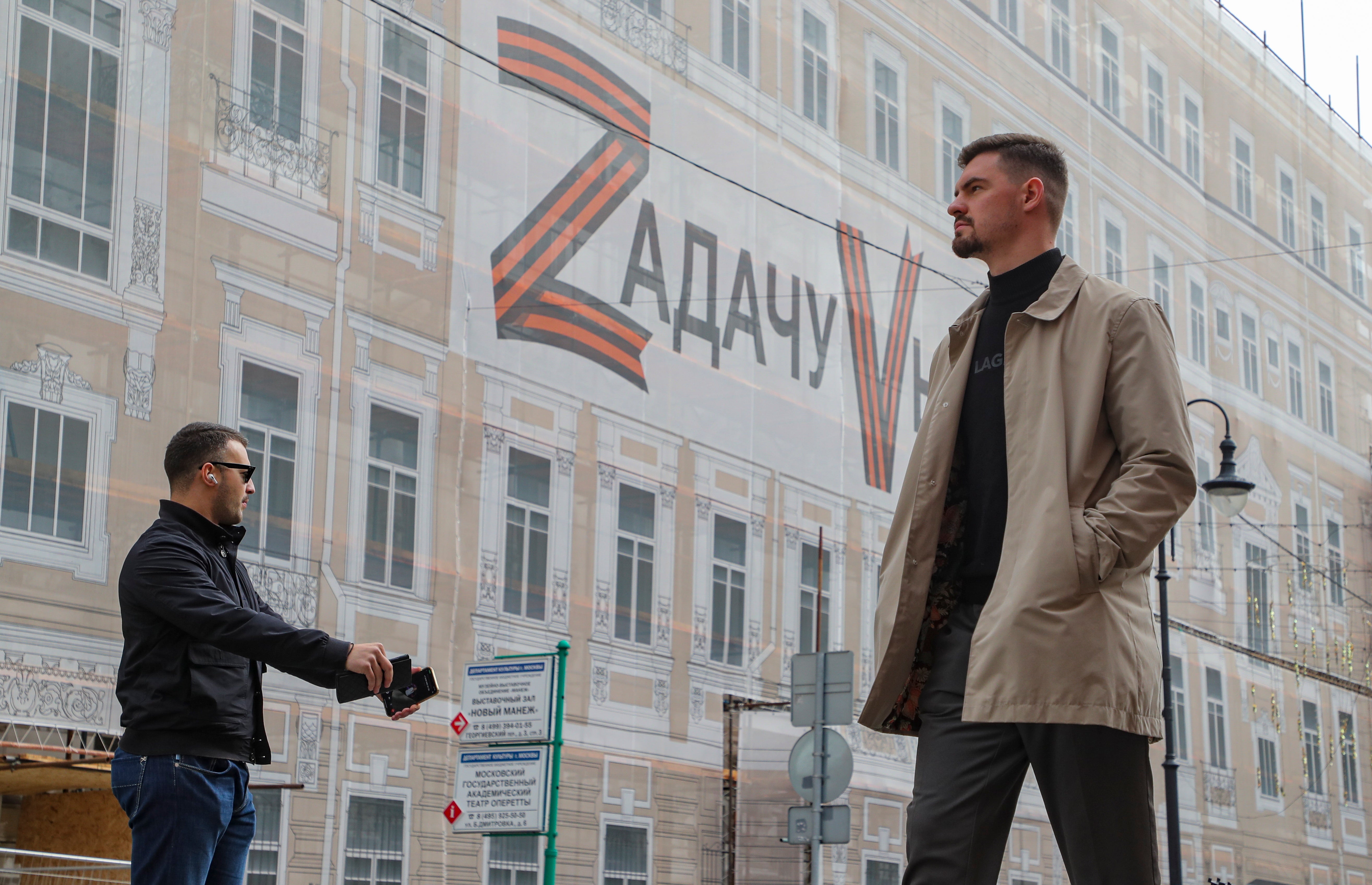 Two men walk near a large banner reading 'The task will be executed' placed on the facade of a building in downtown Moscow