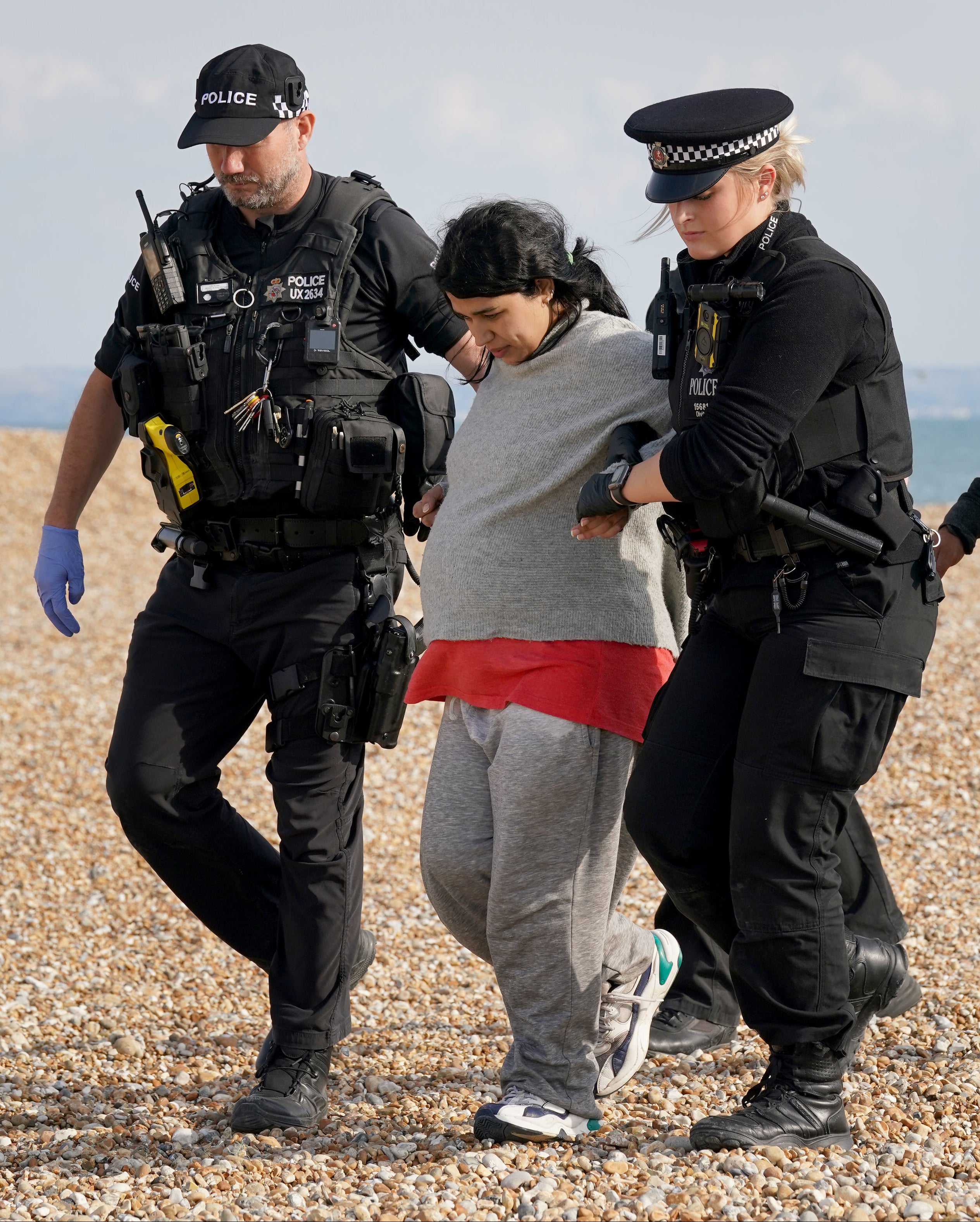 A heavily pregnant lady is helped by police officers as a group of people thought to be migrants walk up the beach in Dungeness, Kent