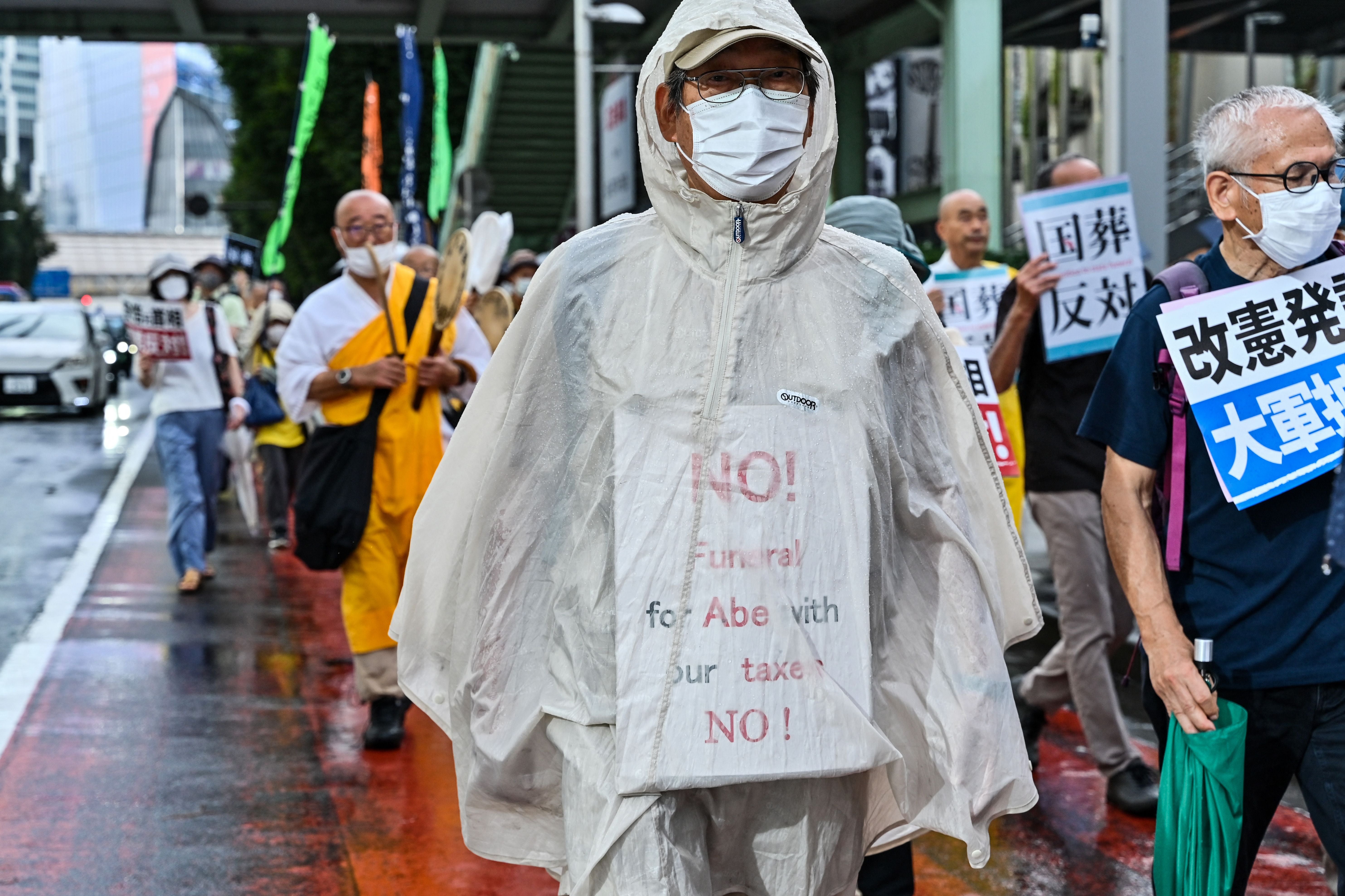 A man wrapped in a rain poncho with an anti-Abe placard takes part in a march with anti-war, anti-nuclear and other protesters against the government’s funding for the funeral of Shinzo Abe