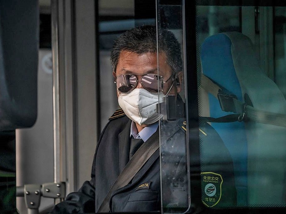 A bus driver wearing a facemask amid the concerns over the Covid-19 coronavirus drives a bus during rush hour on a street in Beijing on 7 April, 2020