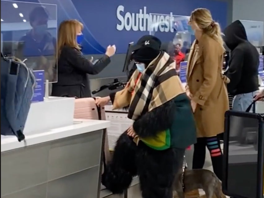 The woman wedging her foot under the suitcase after piling on the costumes and accessories at check-in