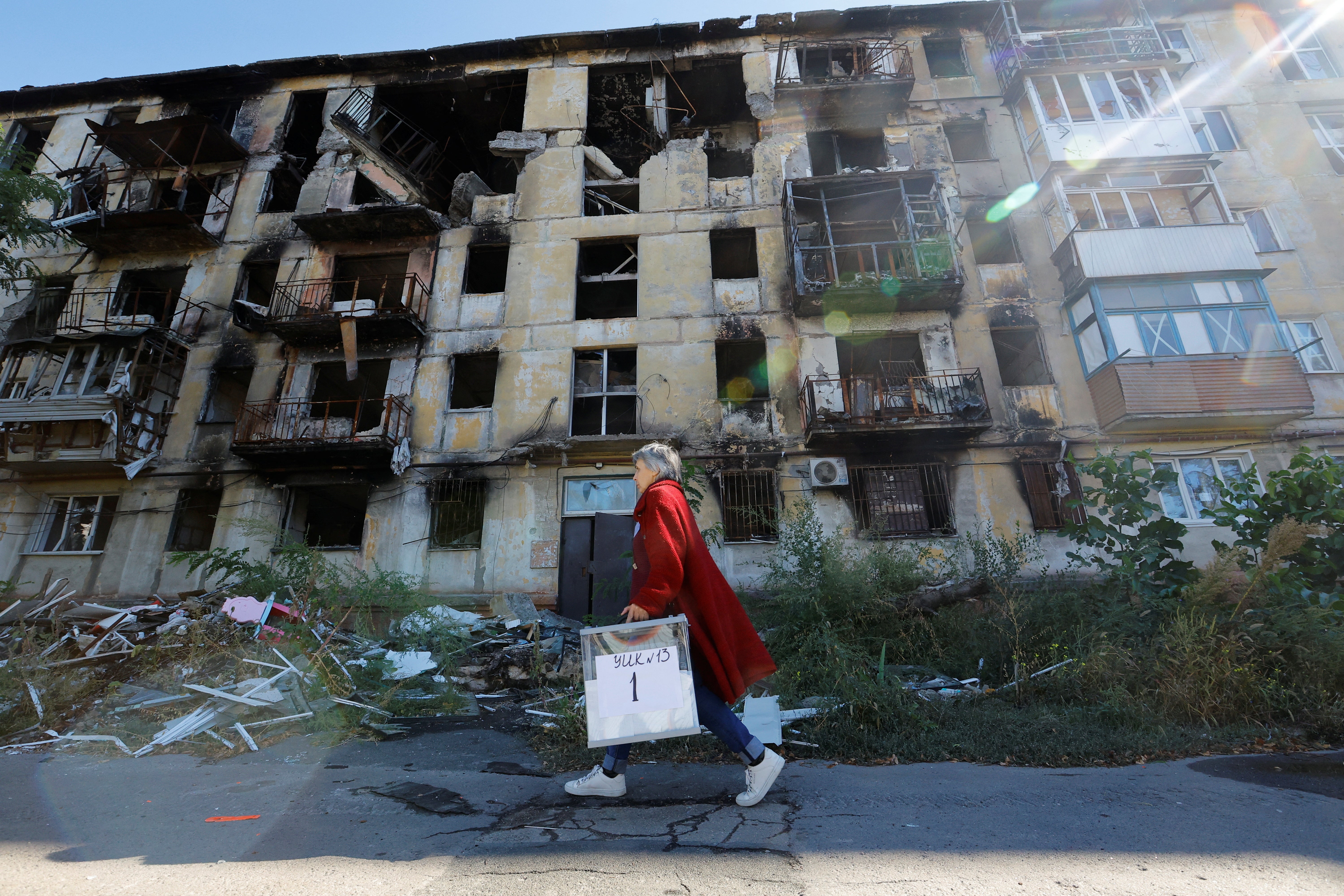 A member of an electoral commission walks past a destroyed building with a mobile ballot box and documents in Mariupol