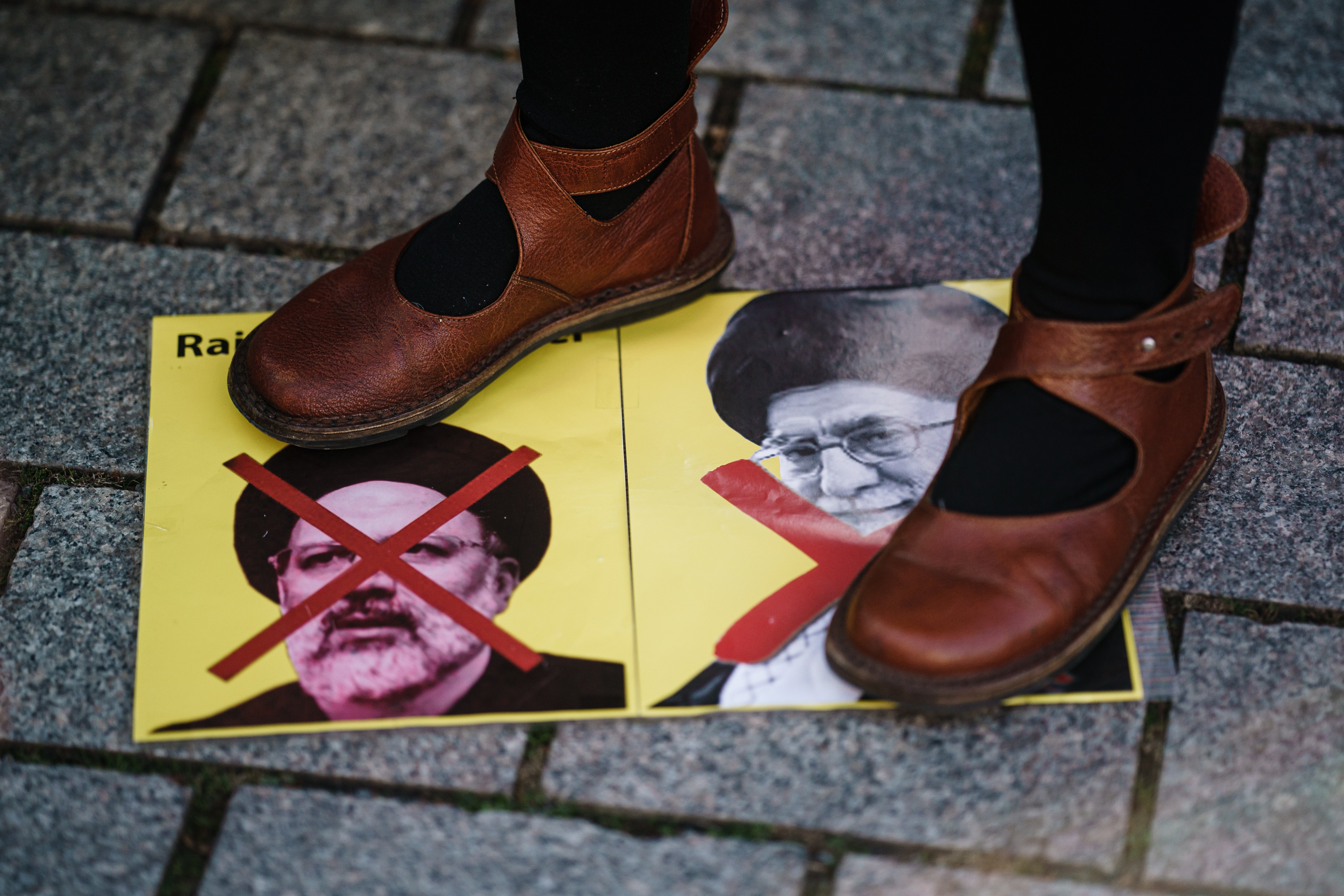 A protester stands on a placard with crossed-out portraits showing Ayatollah Khomeini