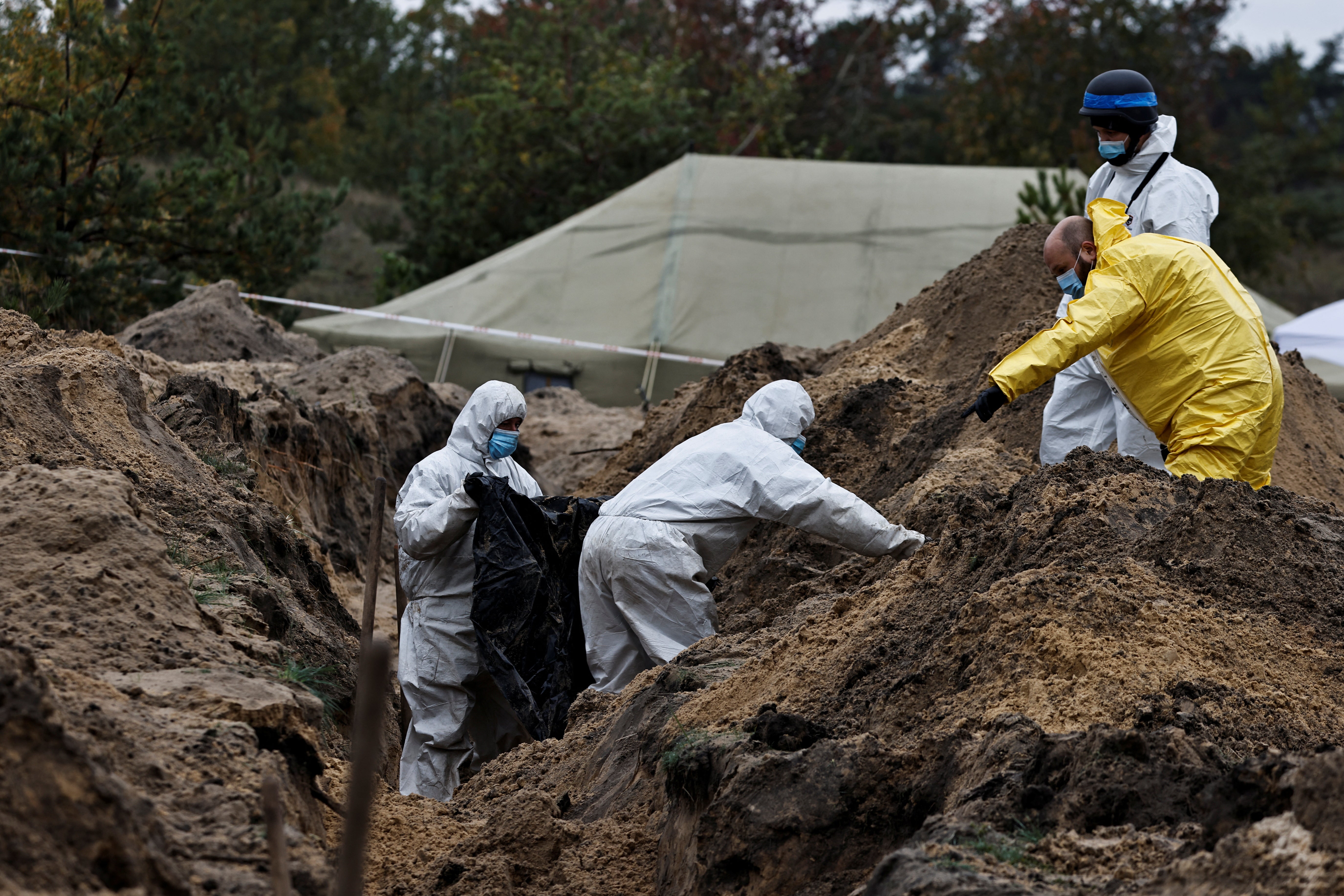 Investigators carry a body they exhumed from a mass grave in Lyman, Donetsk – an area that had been occupied by Russian forces until recently