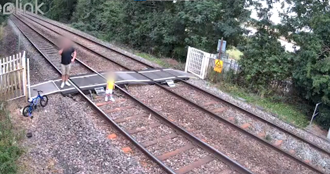 A child stands in the middle of the tracks at a level crossing