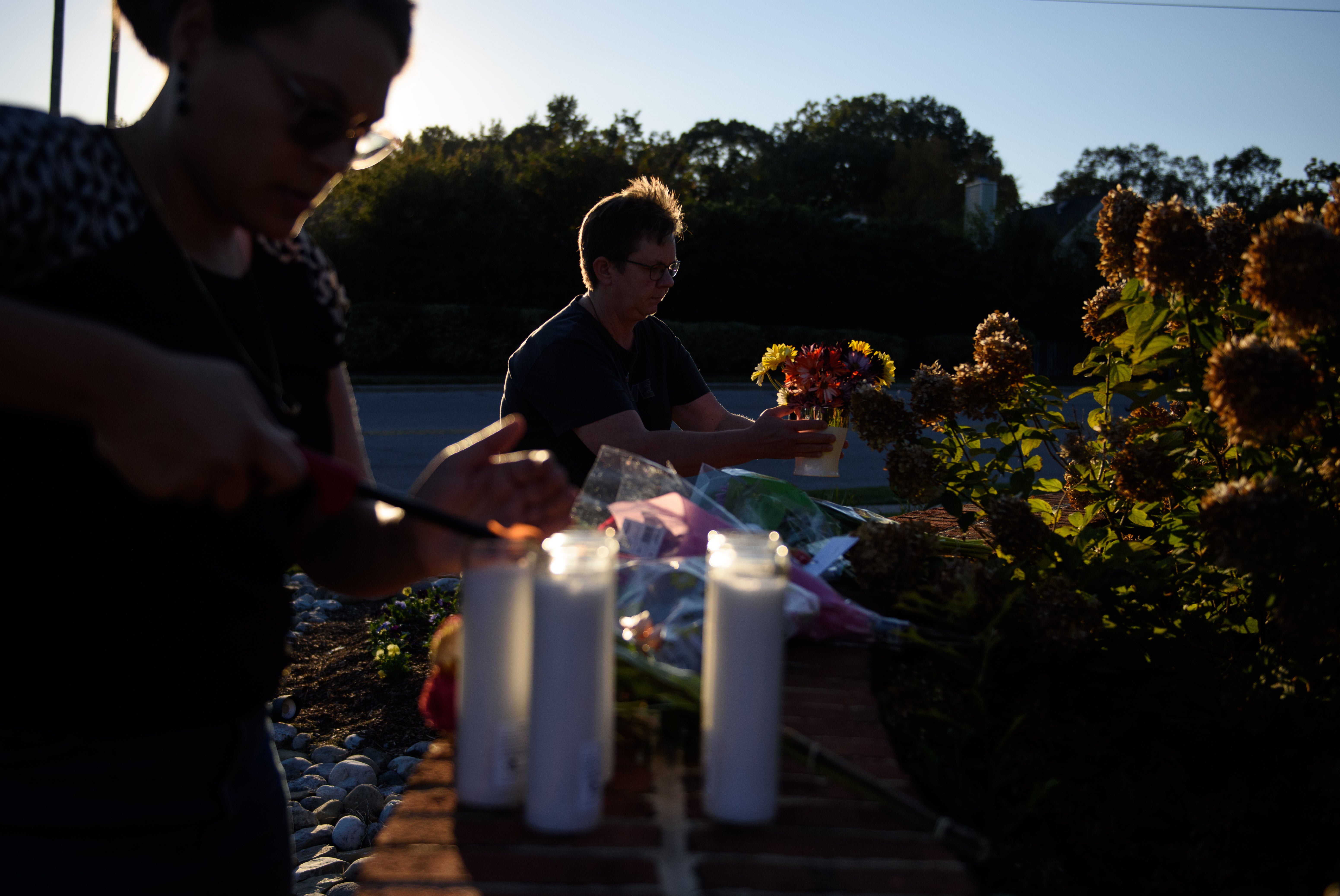 A woman lays flowers while another lights candles at the entrance of Hedingham neighborhood on October 14, 2022 in Raleigh, North Carolina