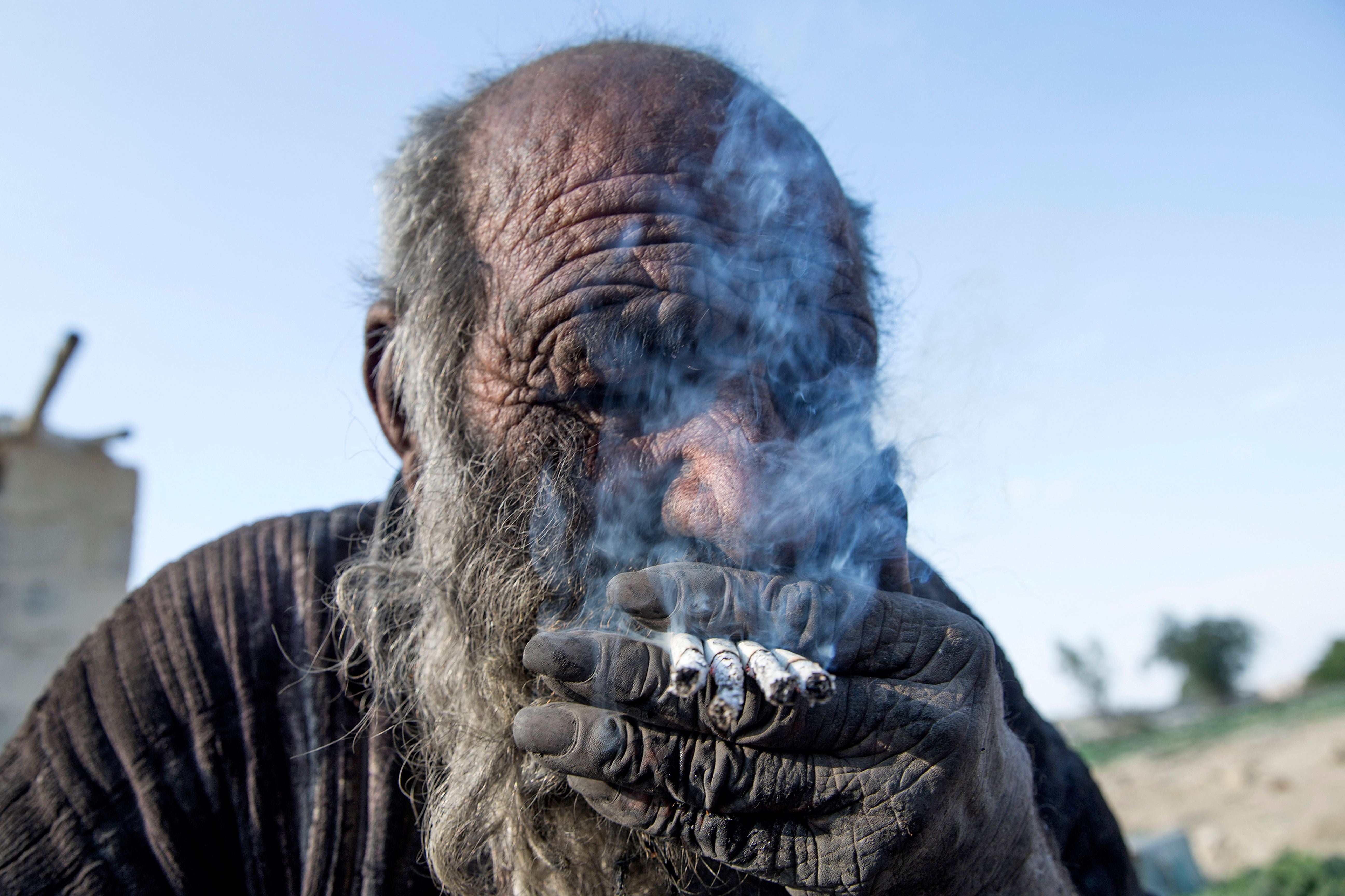 Haji smoking several cigarettes at once by his home in Dezhgah