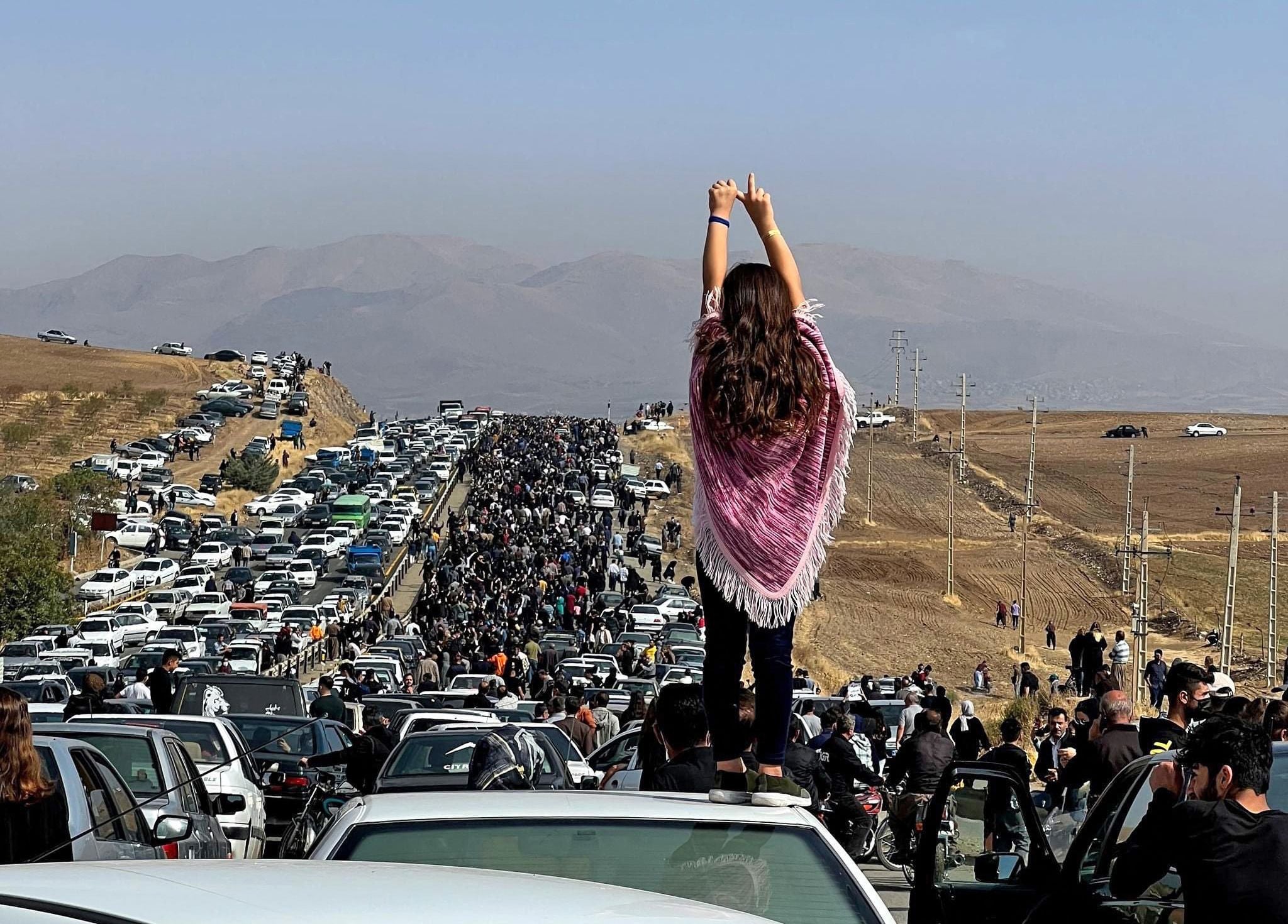 A woman standing on top of a vehicle as thousands make their way towards Aichi cemetery in Saqez, Mahsa Amini’s hometown in the western Iranian province of Kurdistan, to mark 40 days since her death