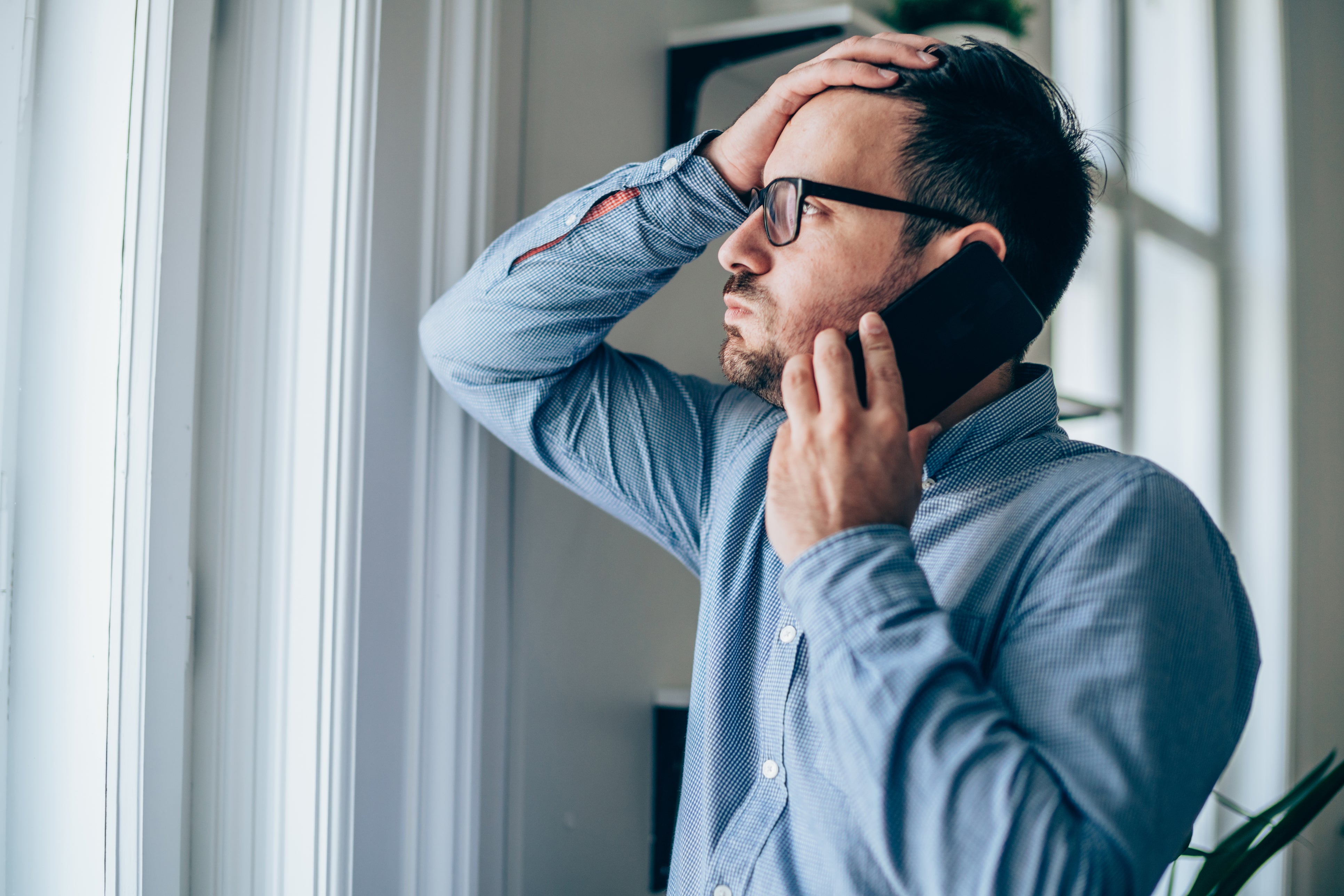 Worried businessman with hand on forehead talking on mobile phone in his office.