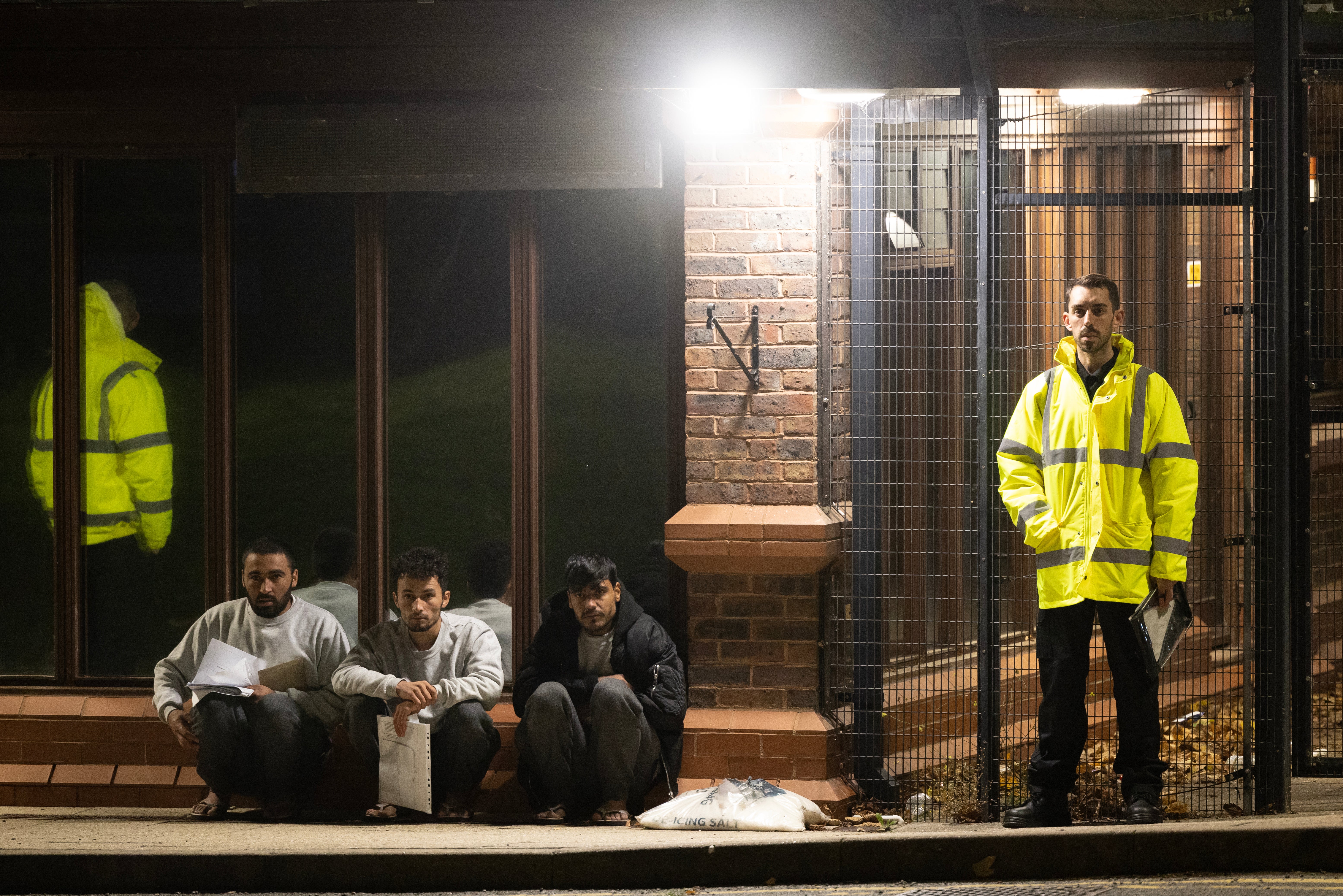 Three Afghan men wait to be dealt with by officials outside a migrant holding facility at Manston Airfield