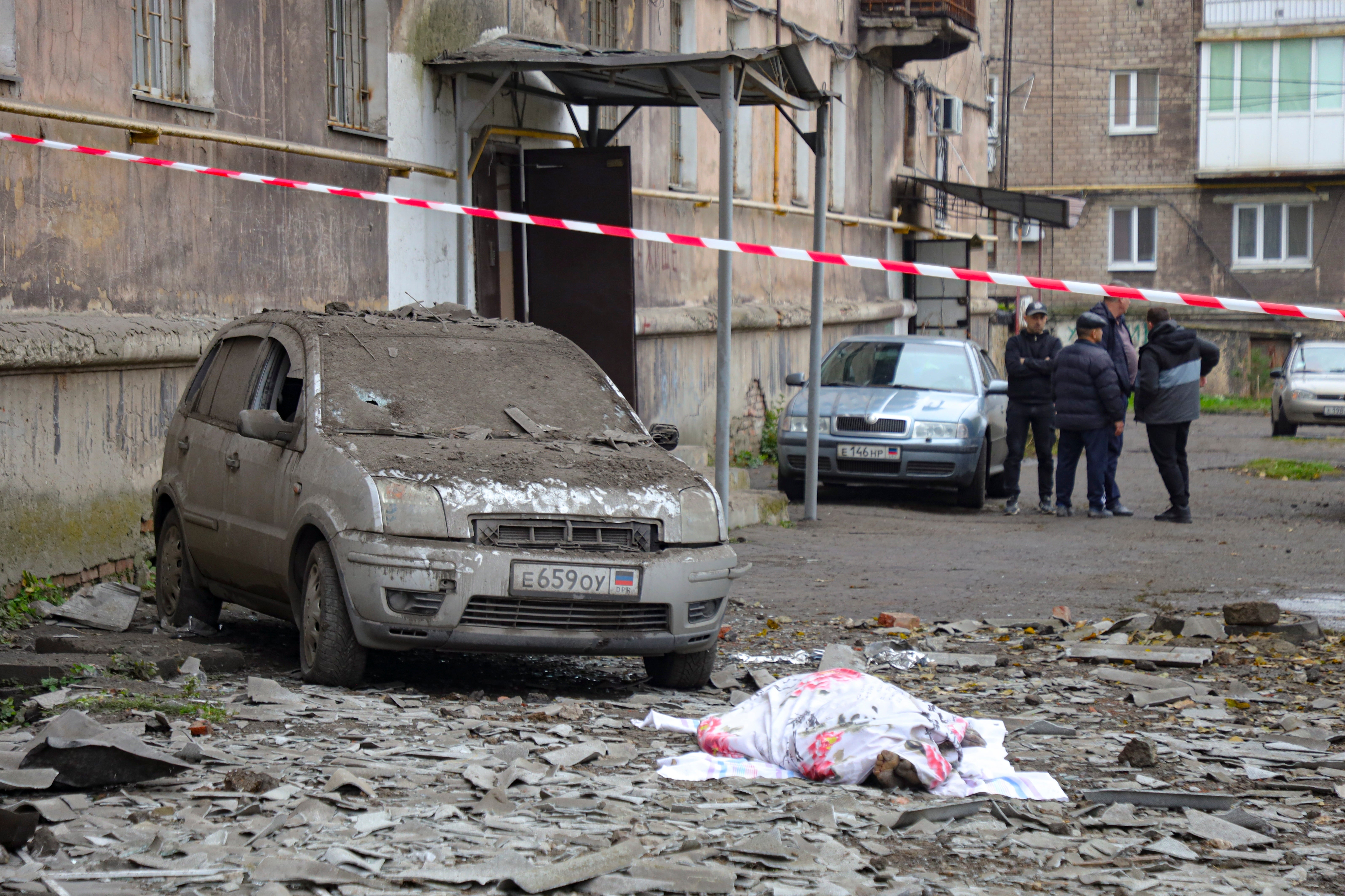 A covered lifeless body lies next to a damaged car after shelling by Ukrainian forces in Makiivka, Donetsk People's Republic, eastern Ukraine