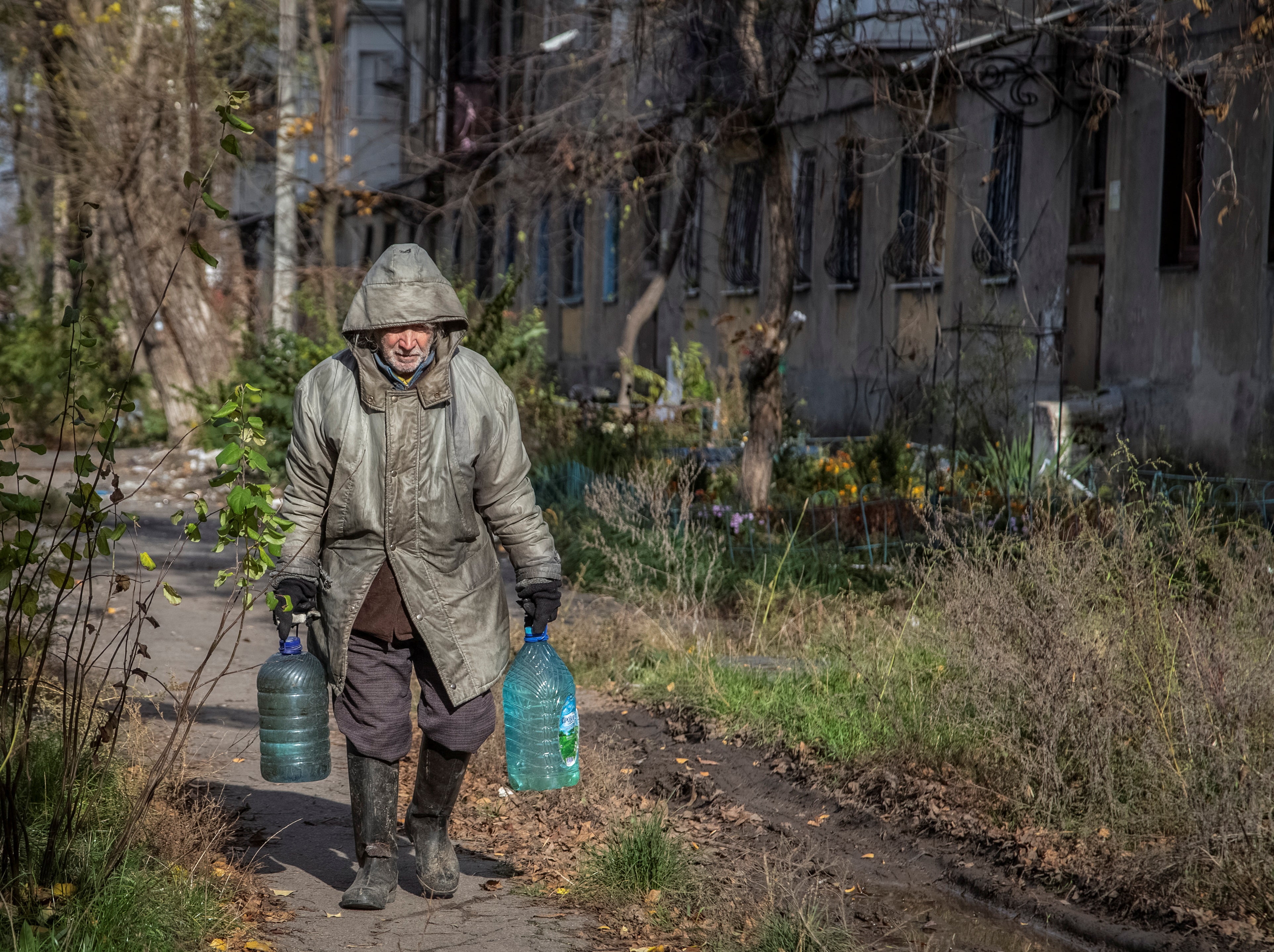 A local resident carries bottles with water near a building destroyed by Russian shelling in Avdiivka, Donetsk