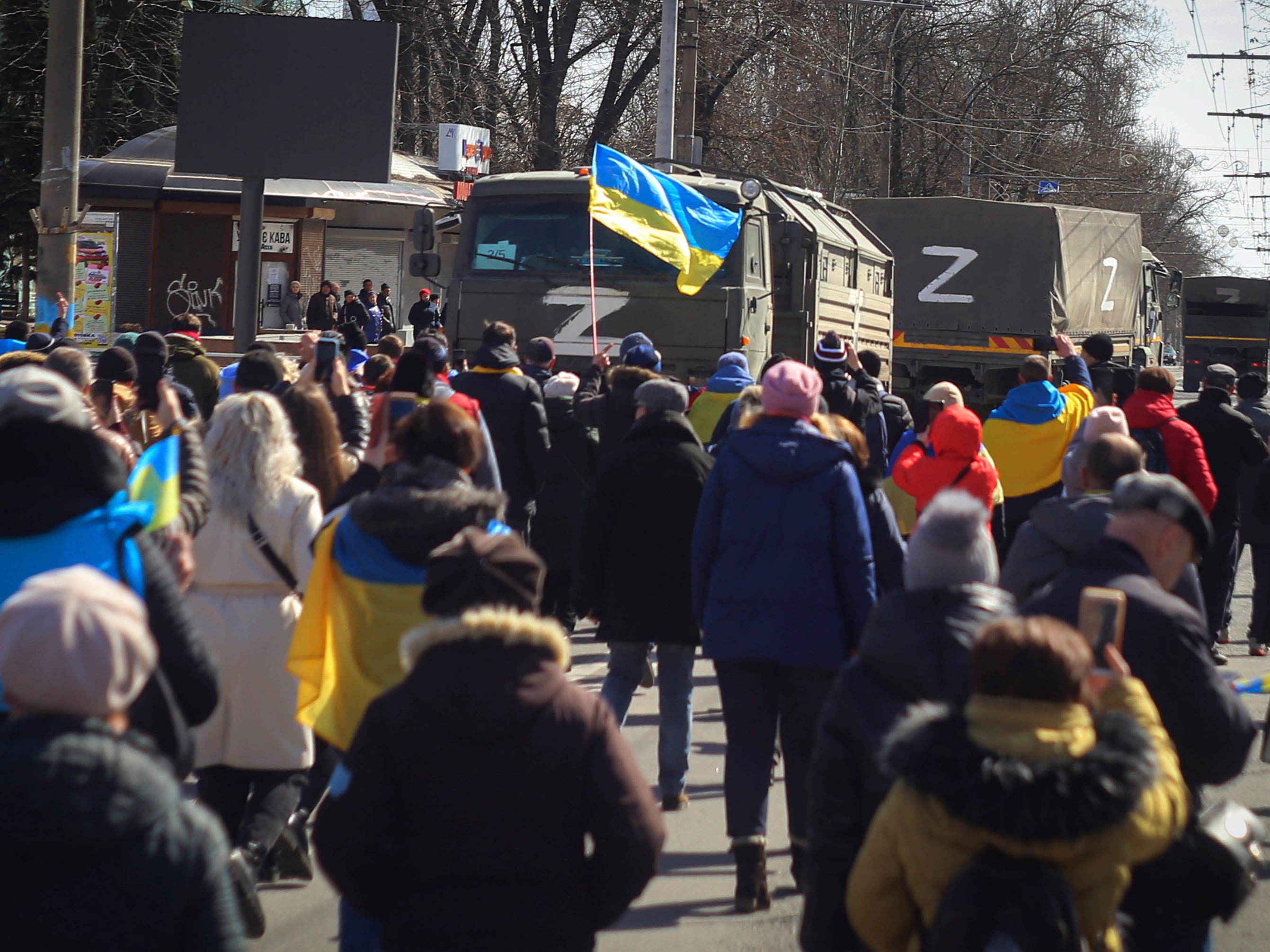 People with Ukrainian flags walk towards Russian army trucks during a rally against the Russian occupation in Kherson