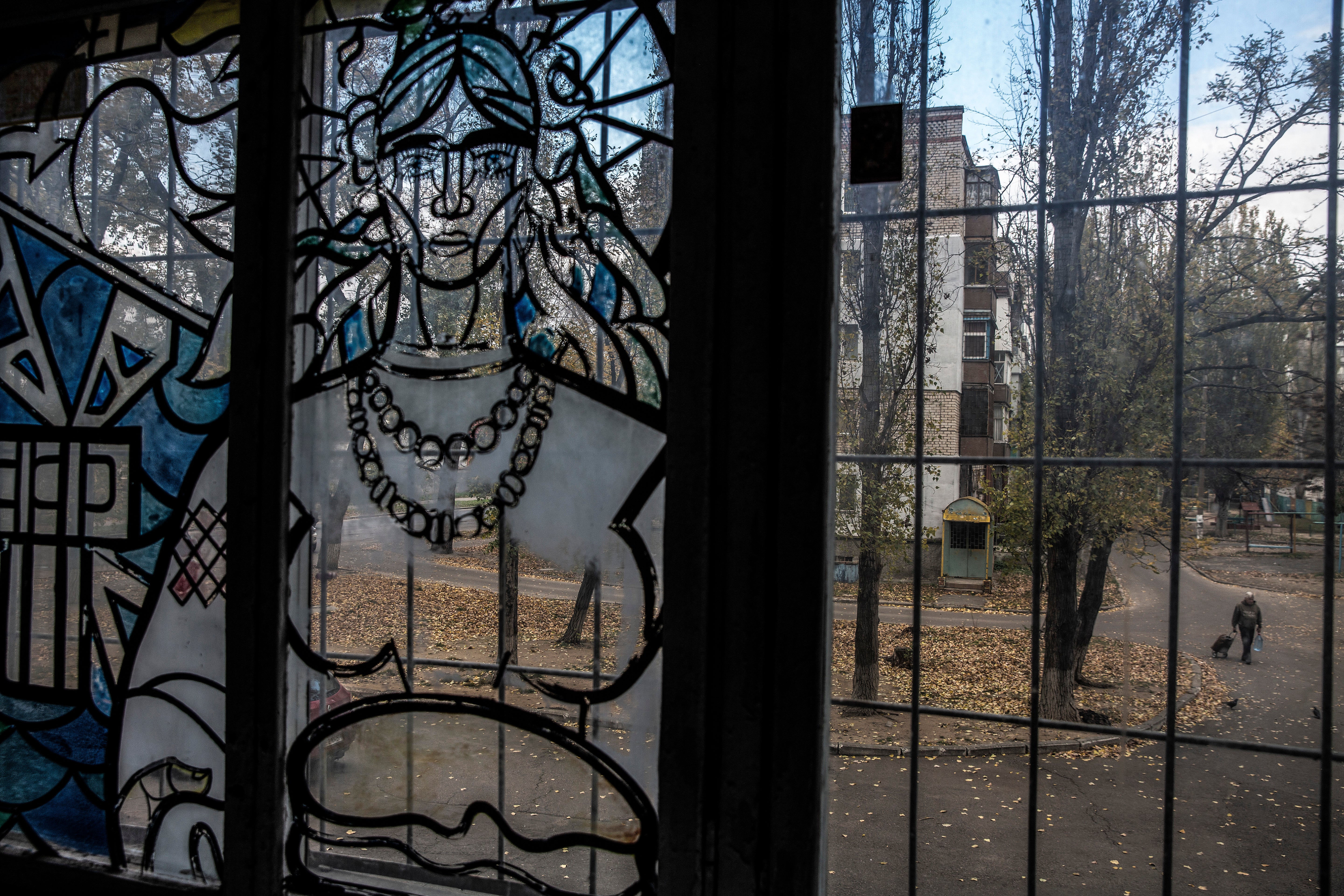 The painted window of an apartment building reveals a woman, in the distance at right, carrying a bottle of water