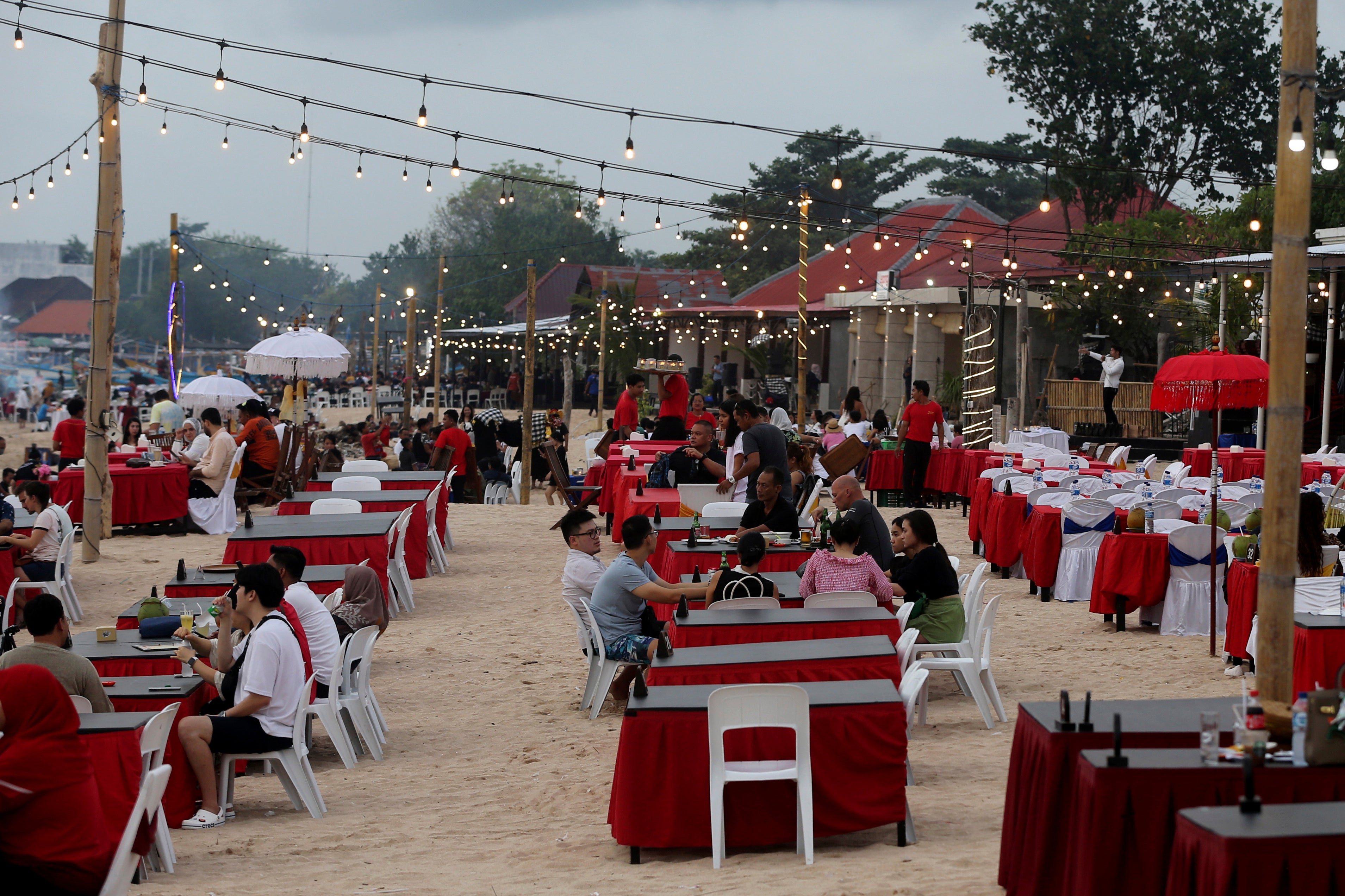 Tourists sit at a restaurant on Jimbaran Beach in Bali, Indonesia