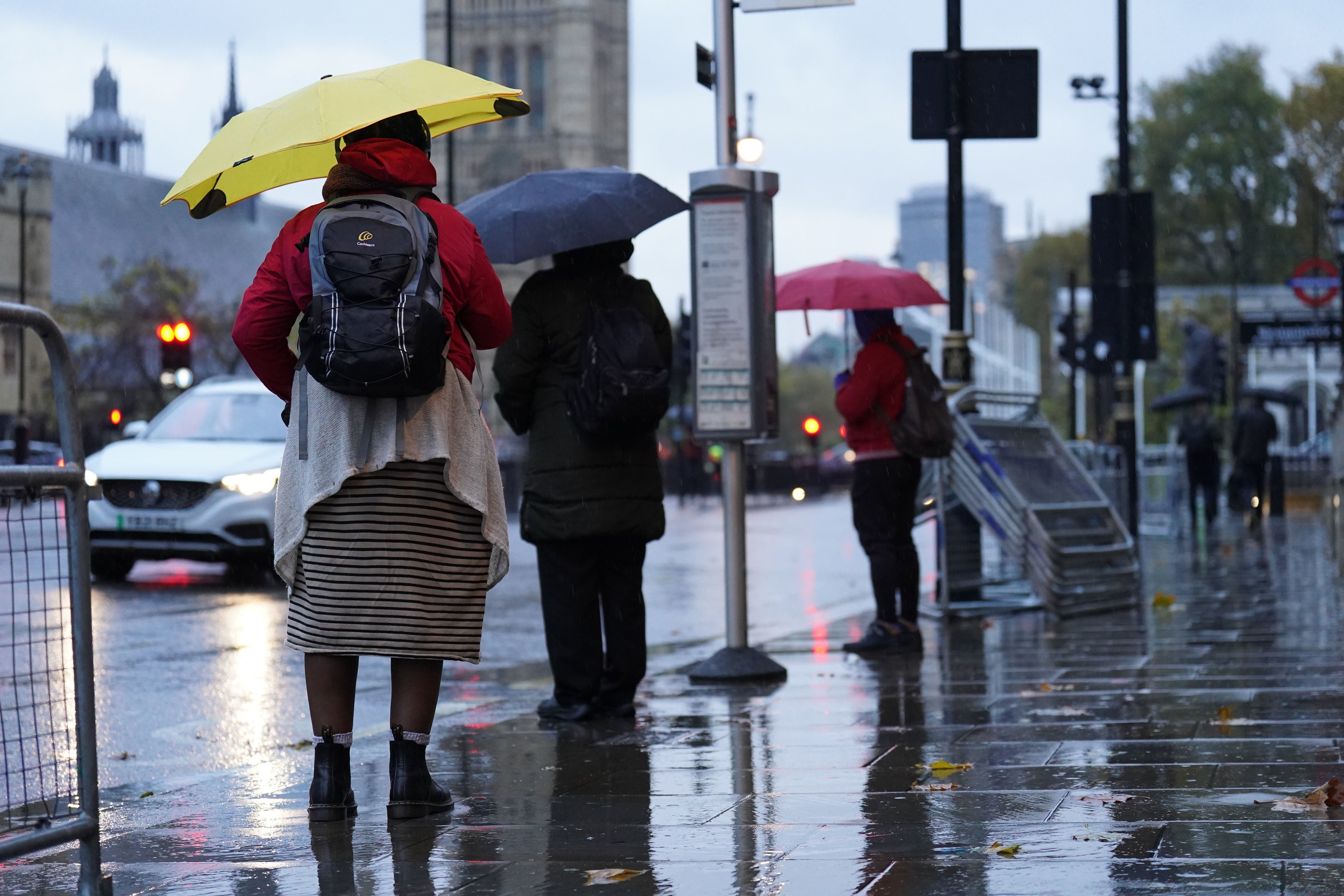 People hold umbrellas as they wait in the rain at a bus stop in Whitehall