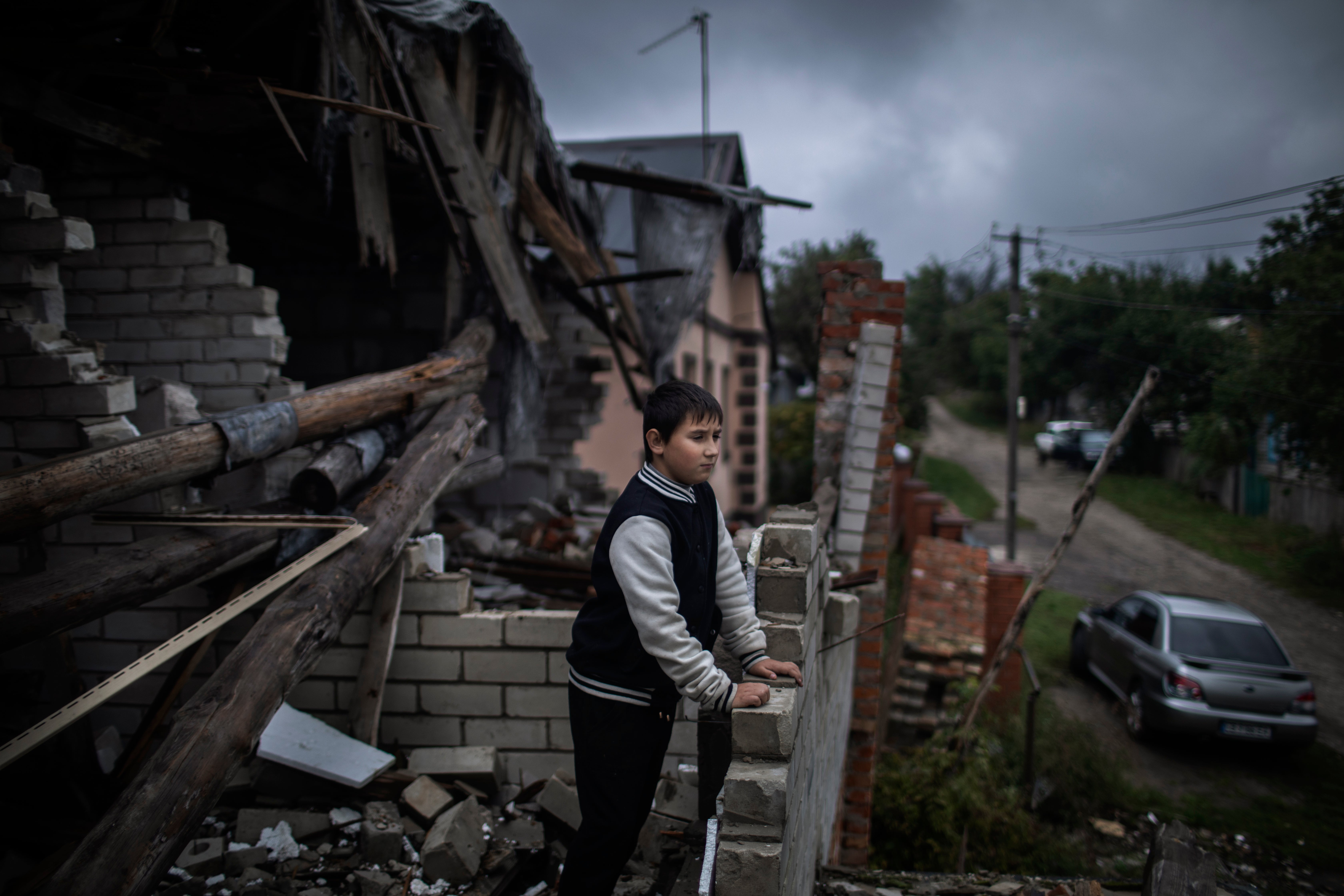 Mykhailo Misha, 9, stands on the ruined roof of his house while he looks at his neighbourhood