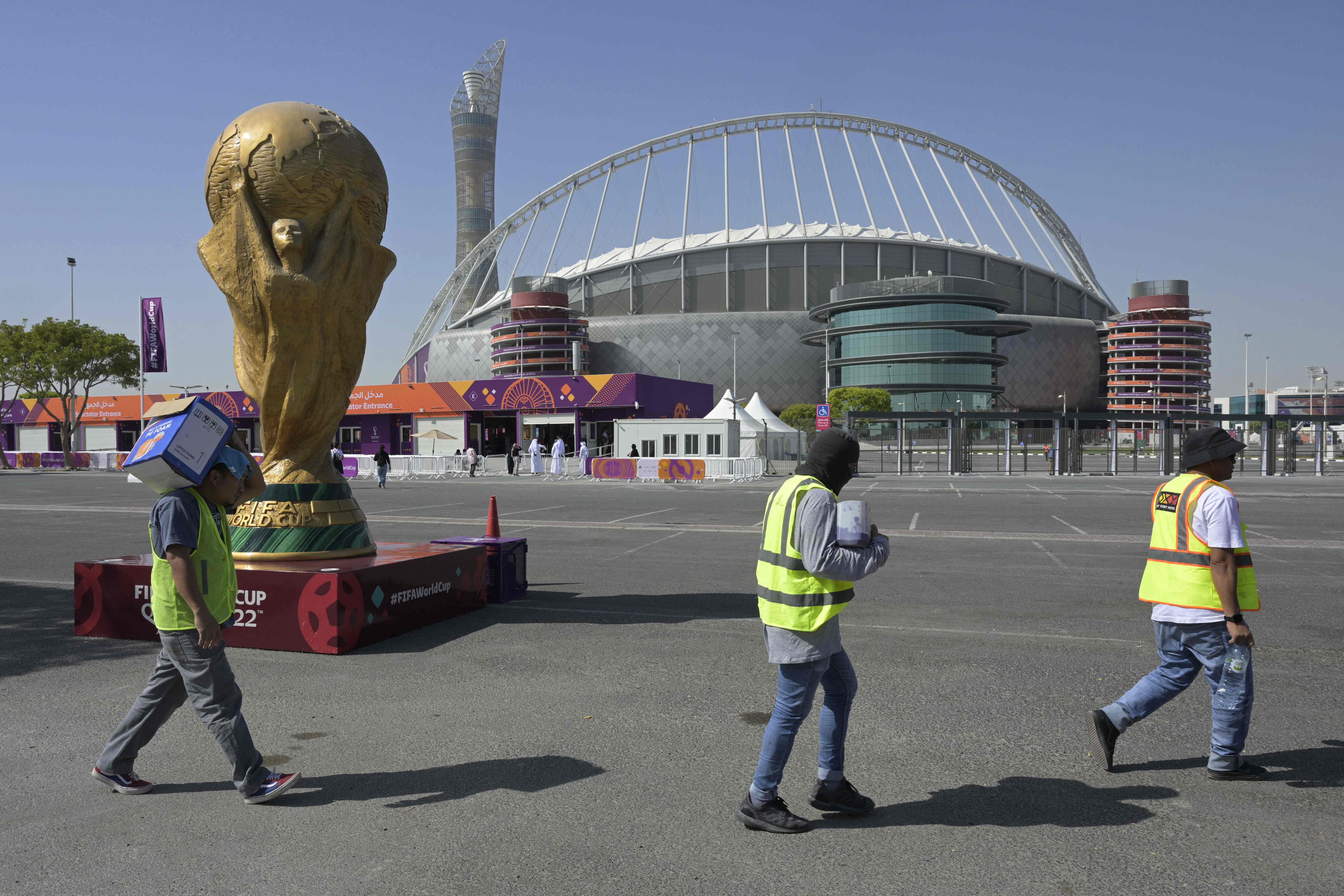 Workers walk past the Khalifa International Stadium in Doha