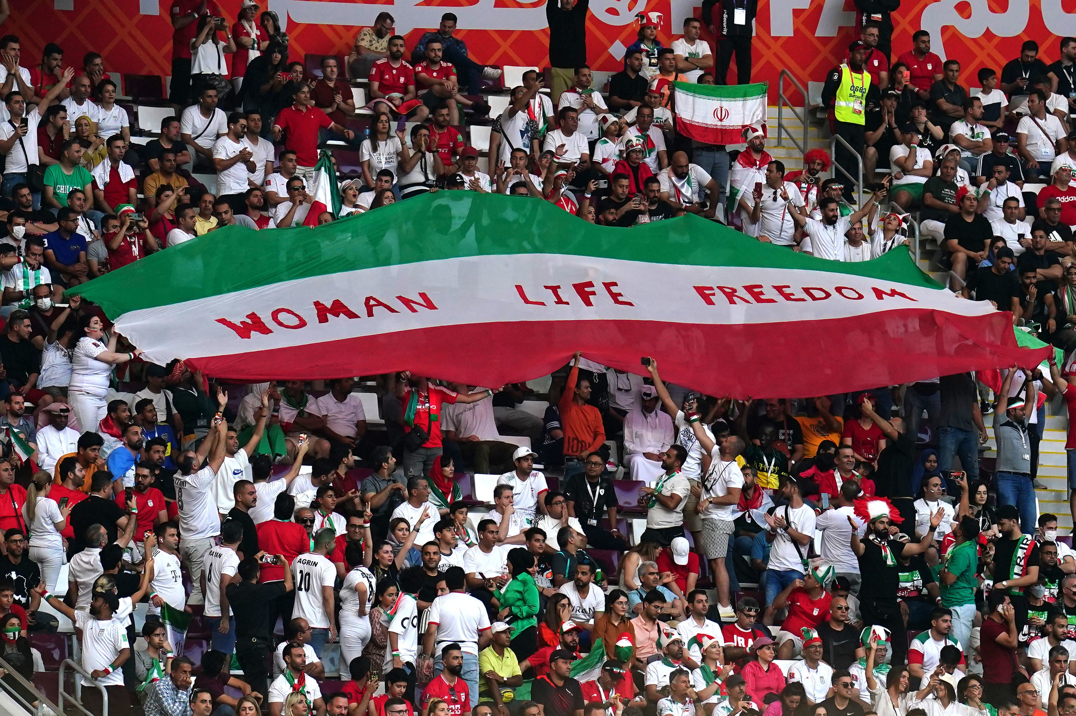 Iran fans in the stands hold up an Iran flag reading “Woman Life Freedom” during the match