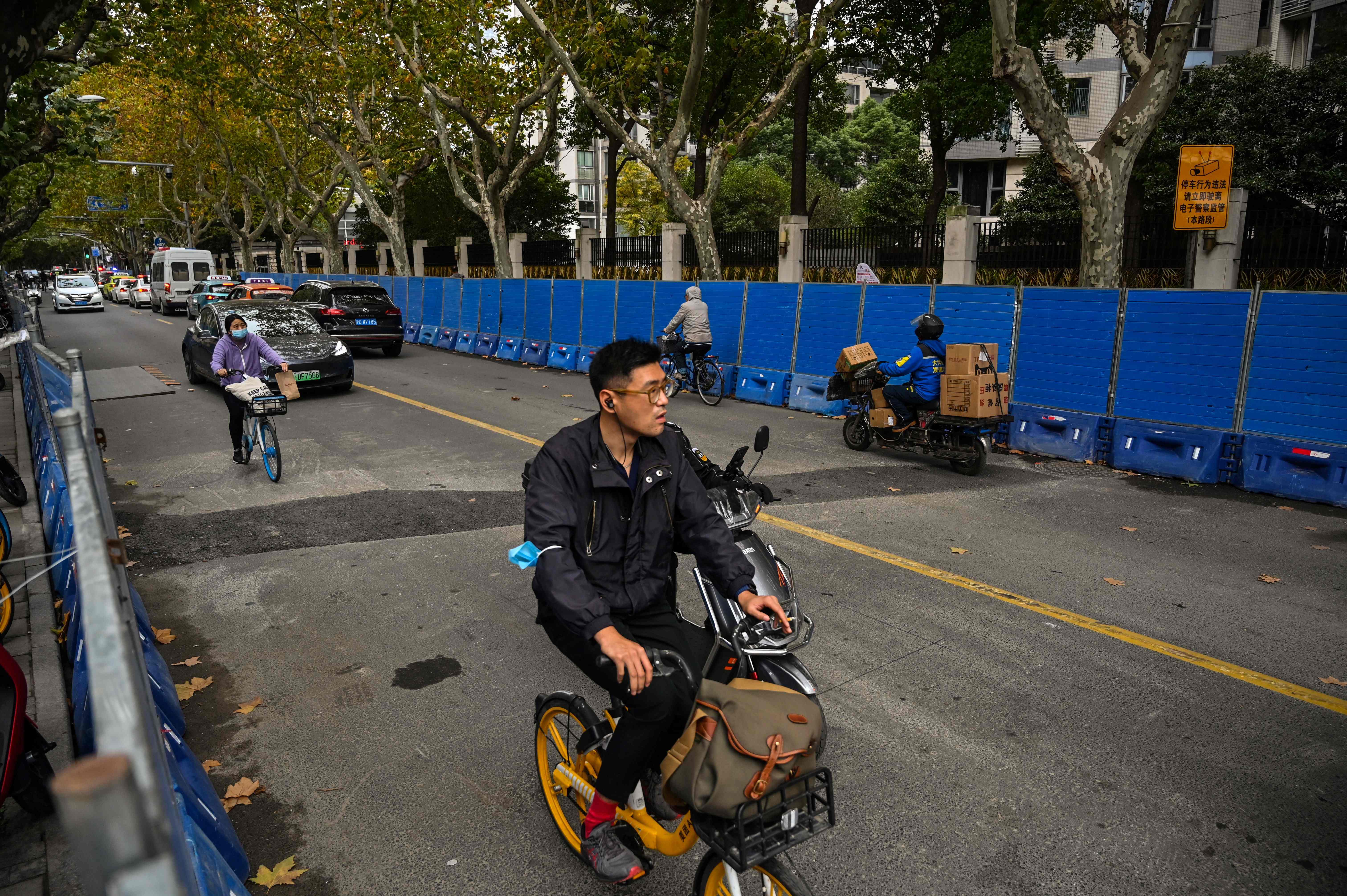 People ride bicycles next to barricades on Wulumuqi street, named for Urumqi in Mandarin, in Shanghai