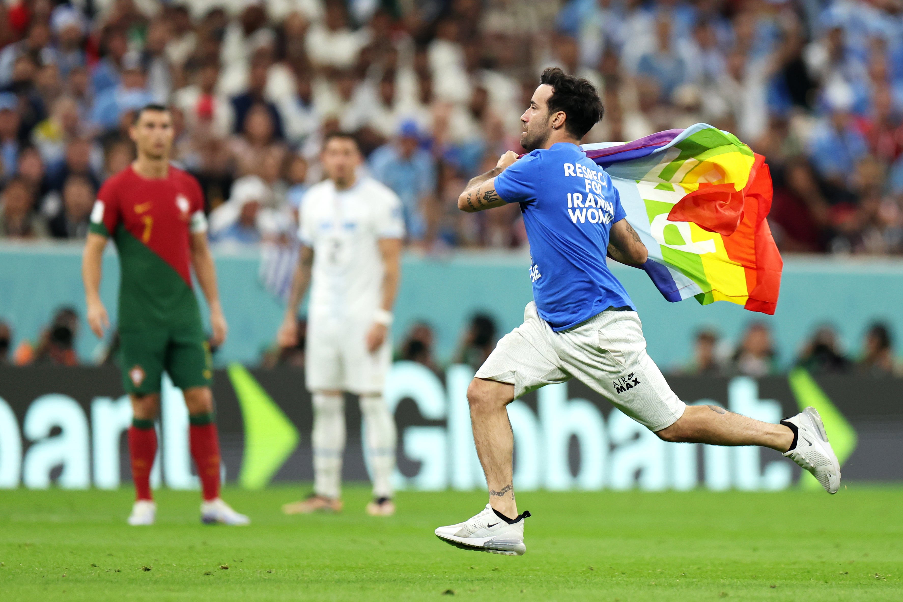 A pitch invader wearing a shirt reading "Respect for Iranian woman" holds a rainbow flag