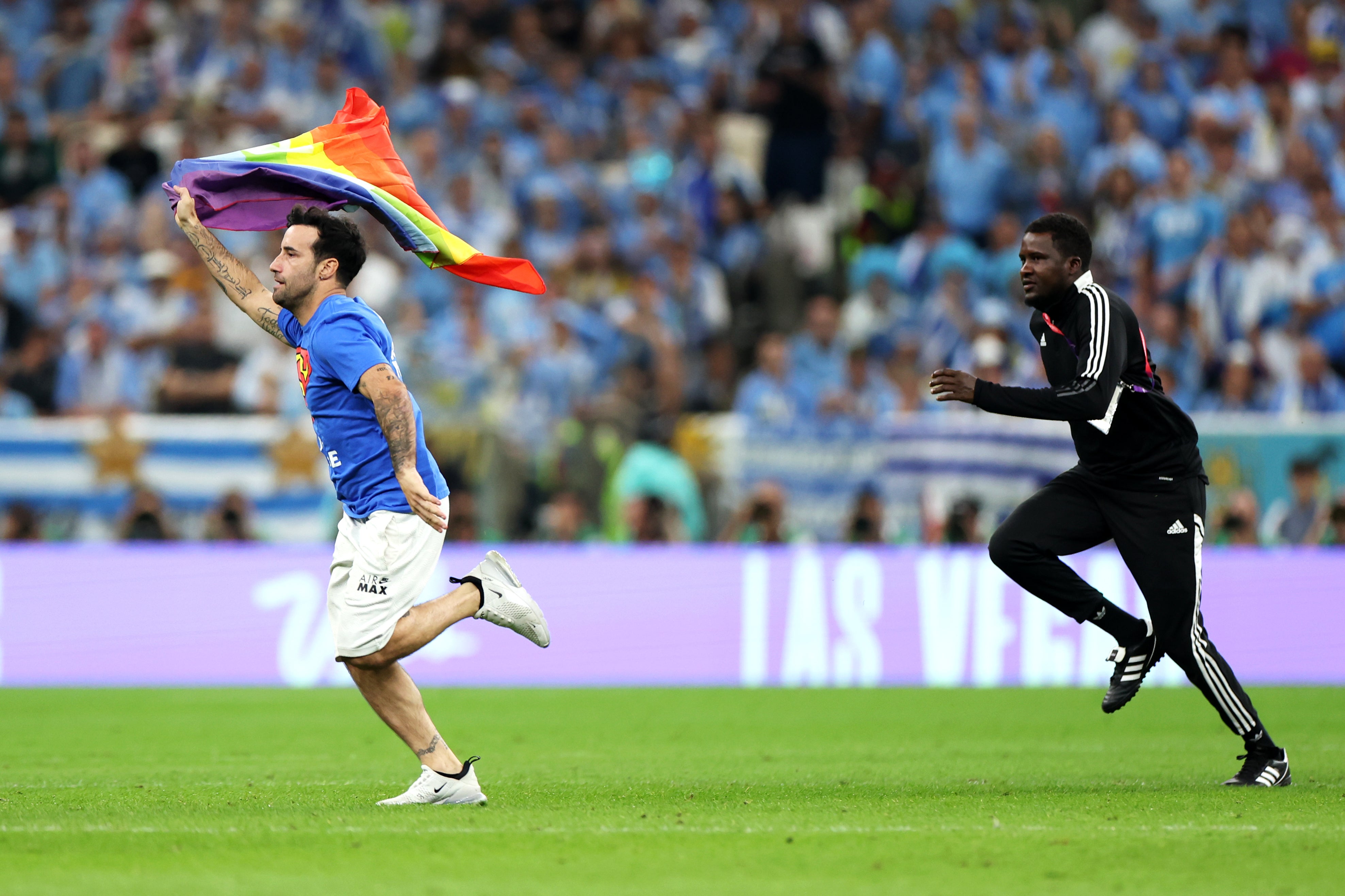 A pitch invader wearing a shirt reading "Save Ukraine" holds a rainbow flag