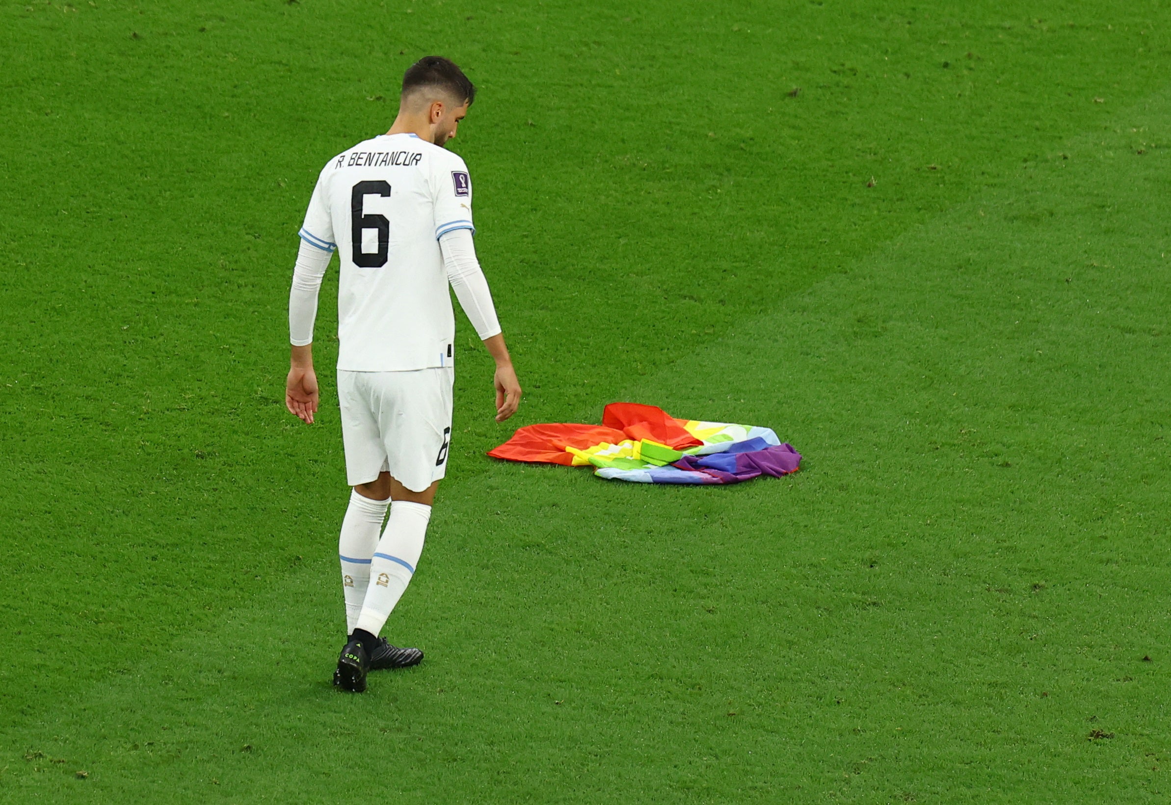 Uruguay's Rodrigo Bentancur and a rainbow flag left behind from a pitch invader