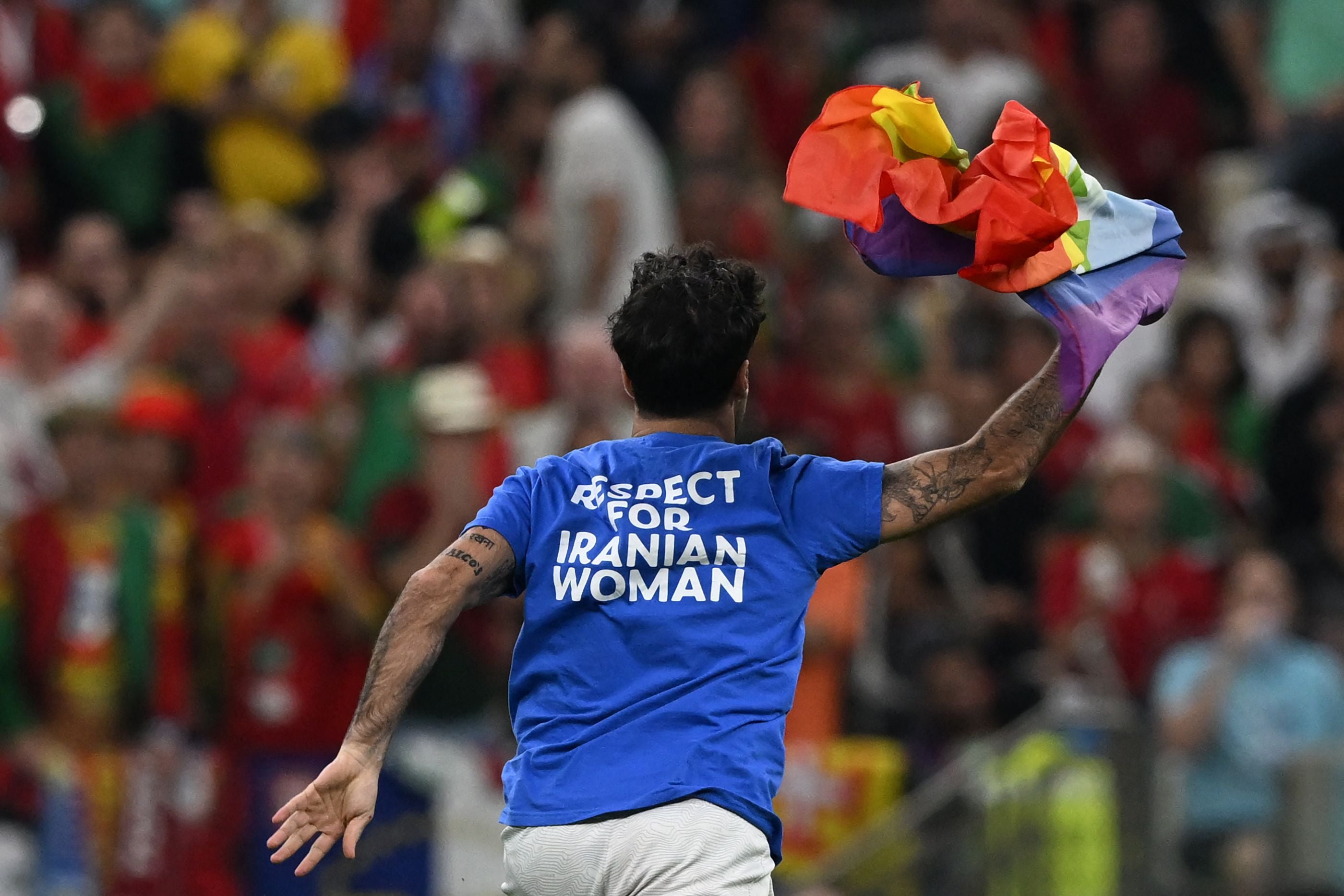 A man wearing a t-shirt reading "Respect For Iranian Woman" runs on the pitch