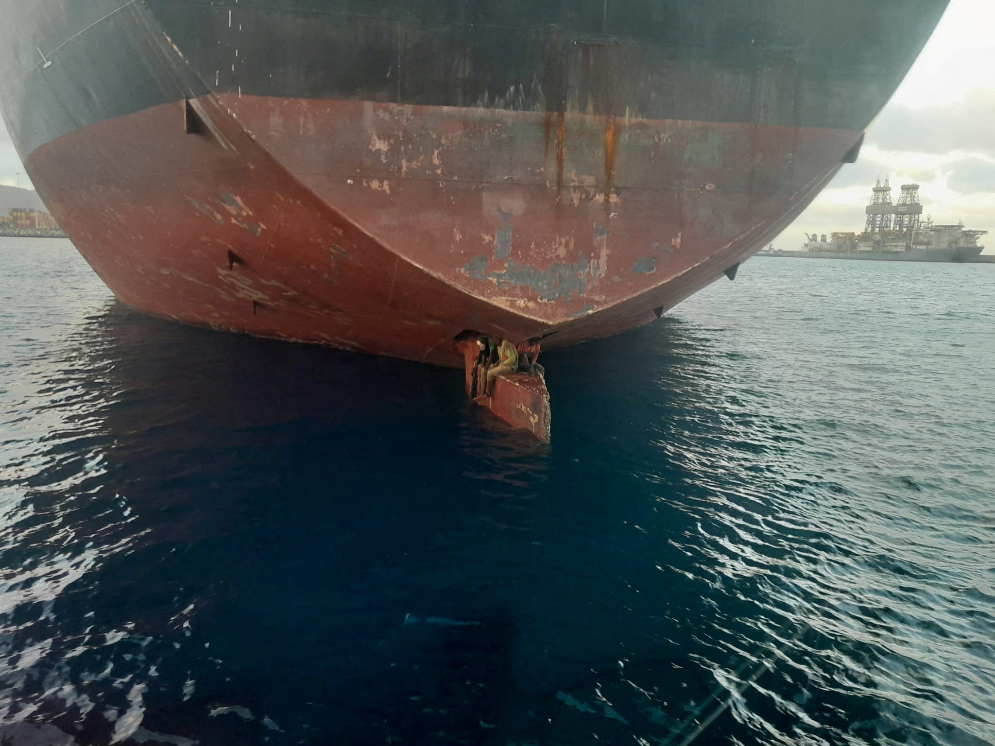 Three stowaway migrants are seen on the rudder blade of petrol vessel Alithini II