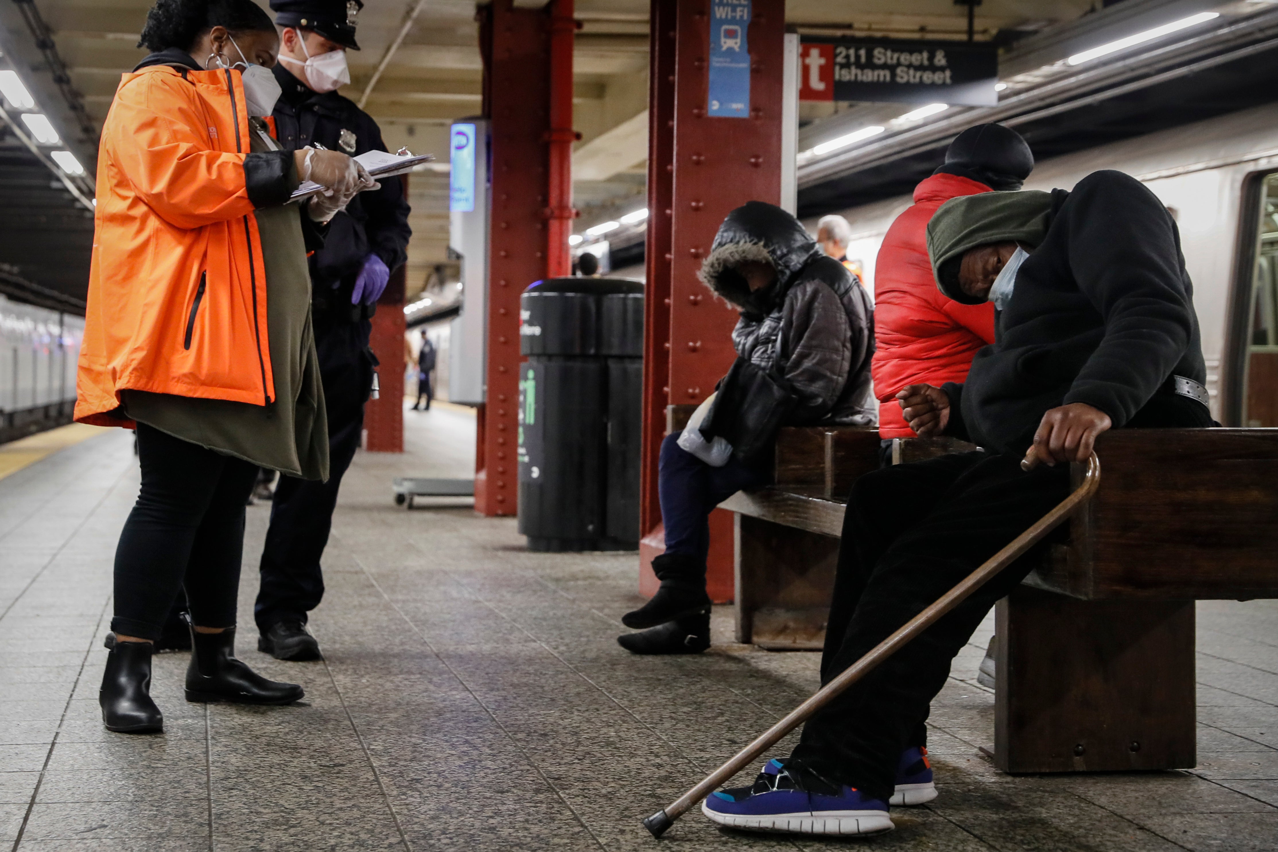 A homeless outreach worker and New York police officer assist people on a subway platform in 2020.